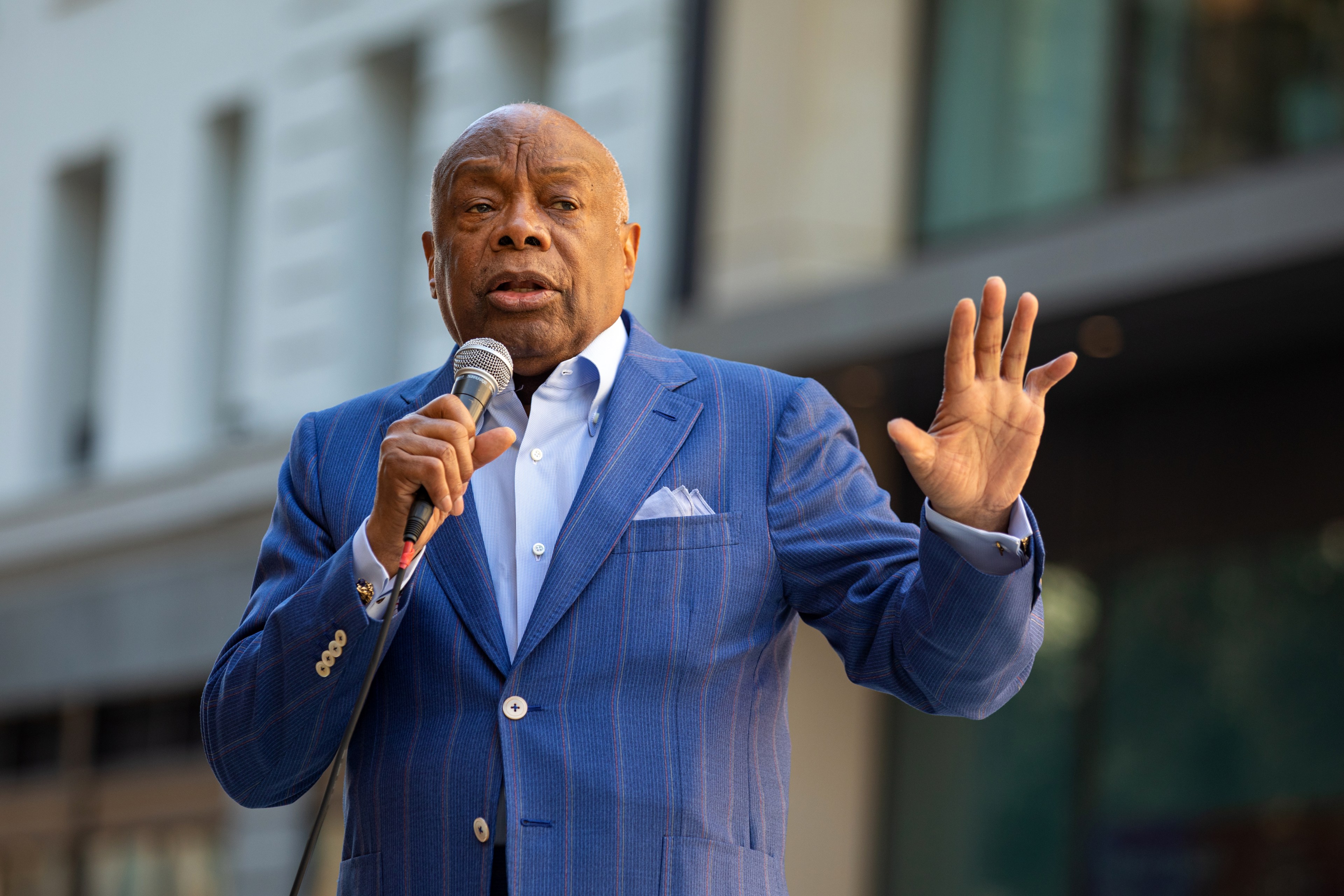 Willie Brown in a suit stands outside with a microphone.