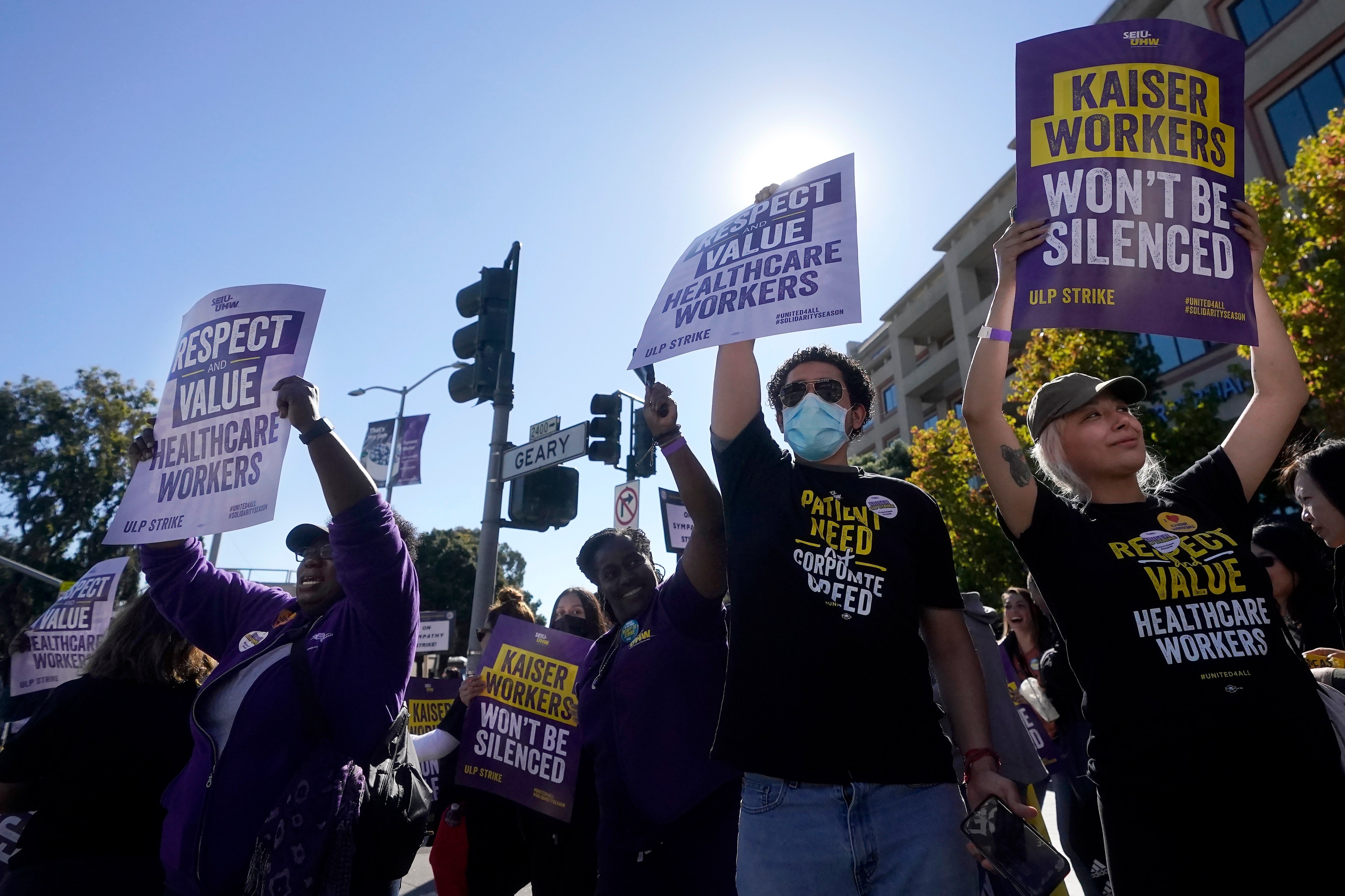 A group of union employees, some wearing masks and sunglasses, hold signs at a public protest.
