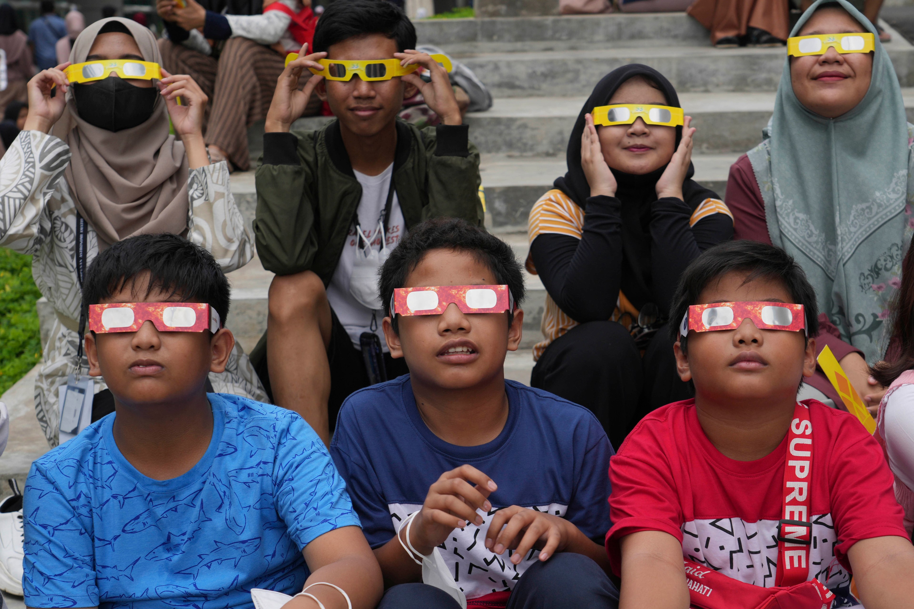 Youths wear protective glasses to watch a hybrid solar eclipse in Jakarta, Indonesia, Thursday, April 20, 2023.