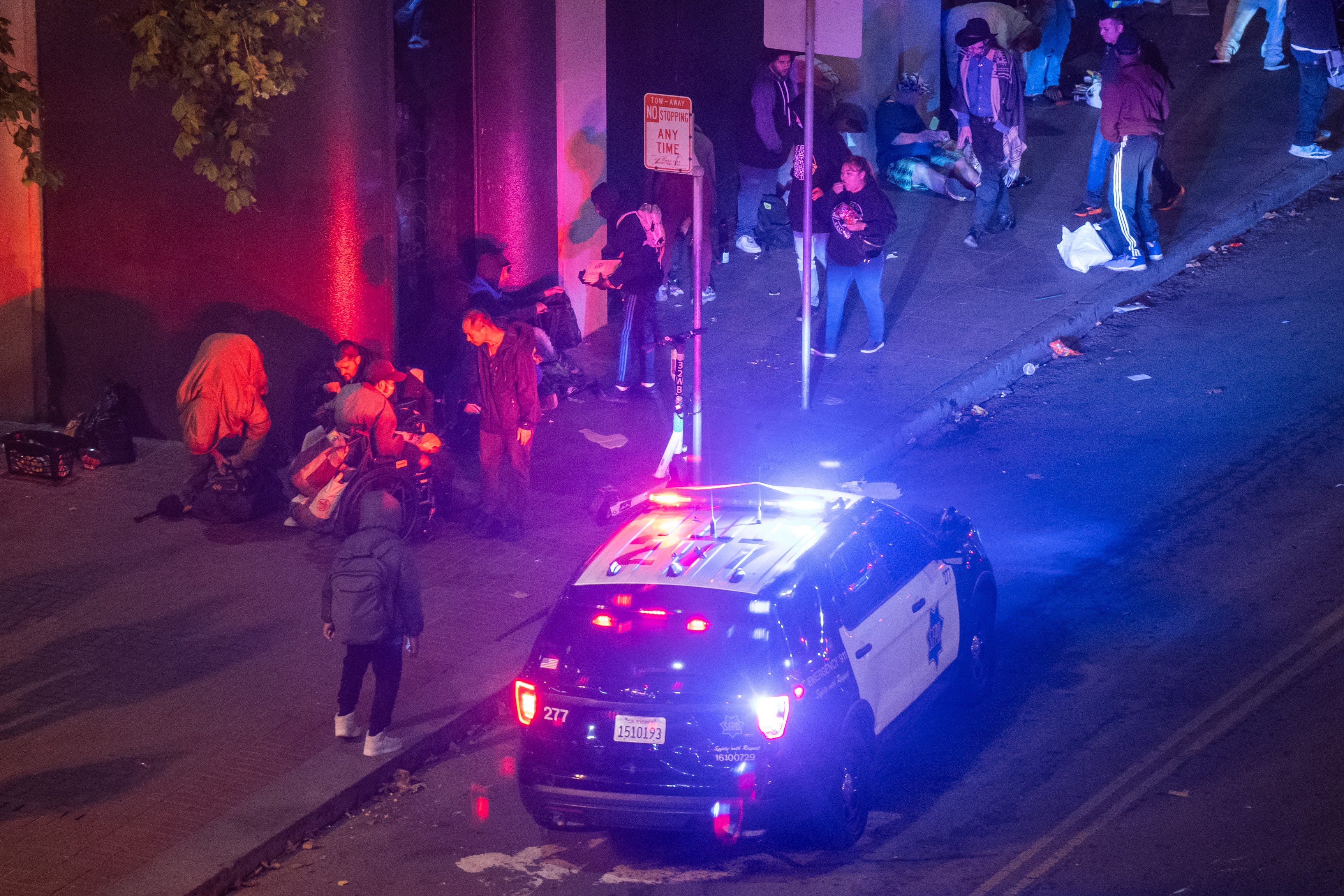 A police car shines its lights next to a crowd of people.