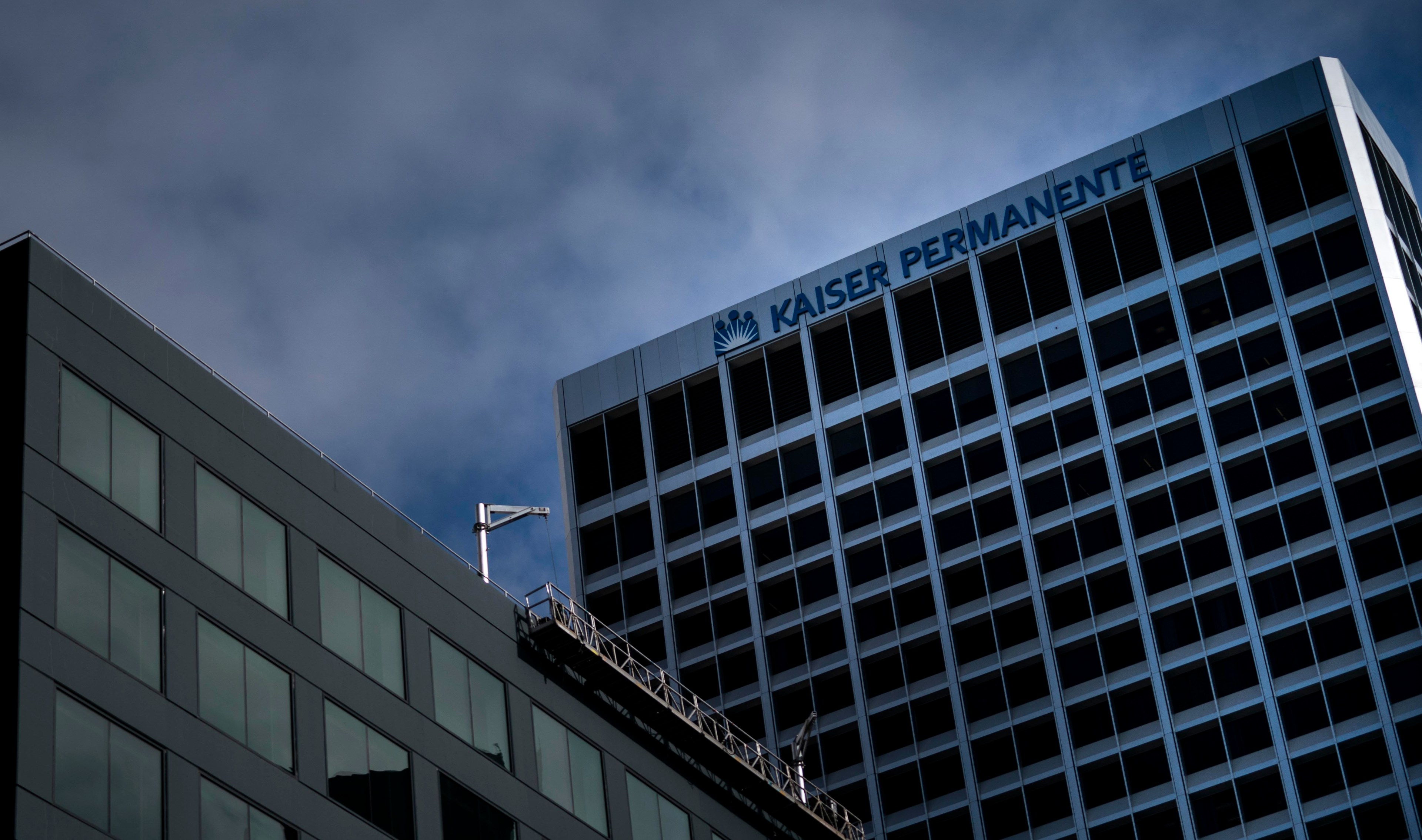 The Kaiser Permanente logo is seen on a building, with a gray, cloudy sky in the background