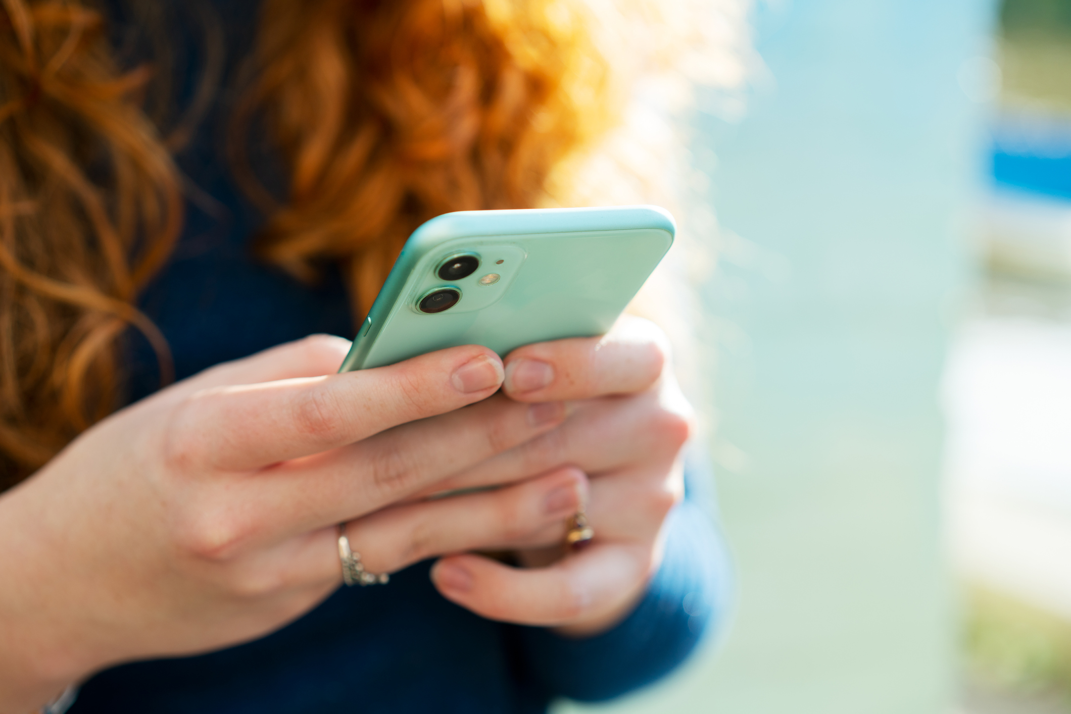 A stock photo shows a woman with long curly red hair using a pale green cell phone.