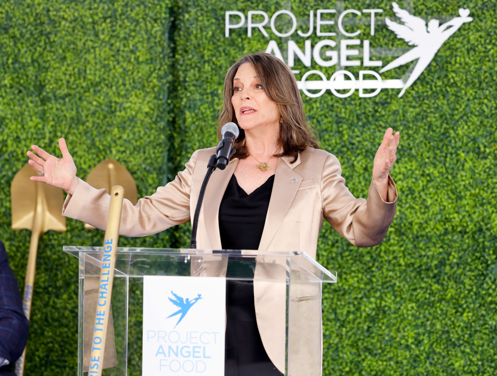 A woman is speaking at a podium with the "Project Angel Food" logo behind her, gesturing with her hands.