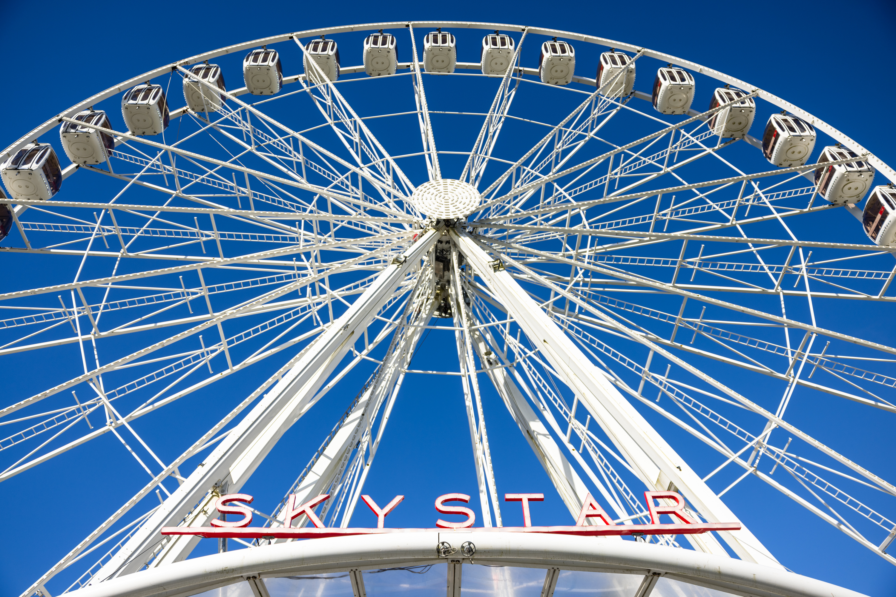 A large white Ferris wheel named "SKY STAR" under a clear blue sky, with enclosed gondolas on the rim.
