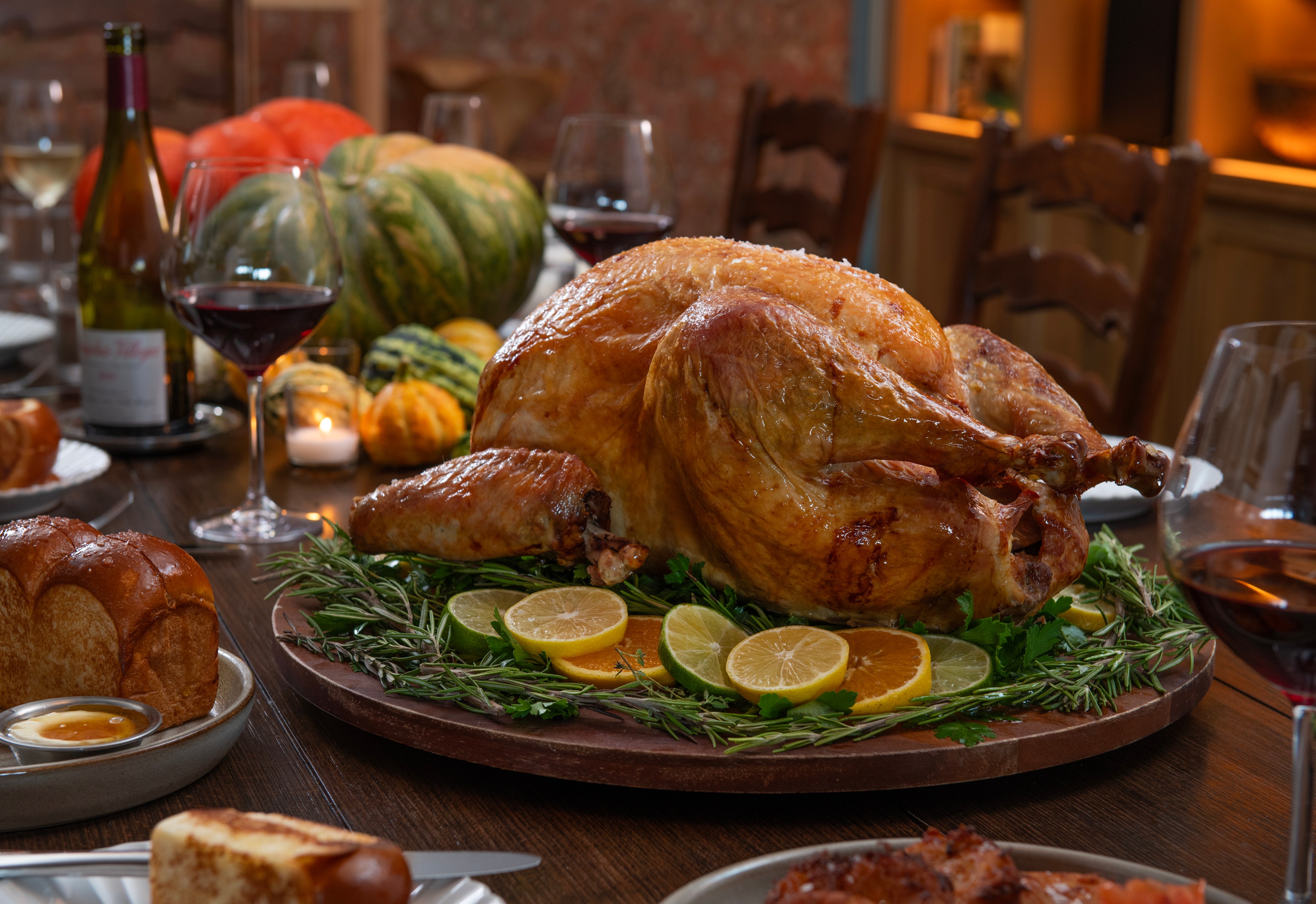 A picture of a whole cooked turkey on a dinner table full of dishes, including bread and wine.