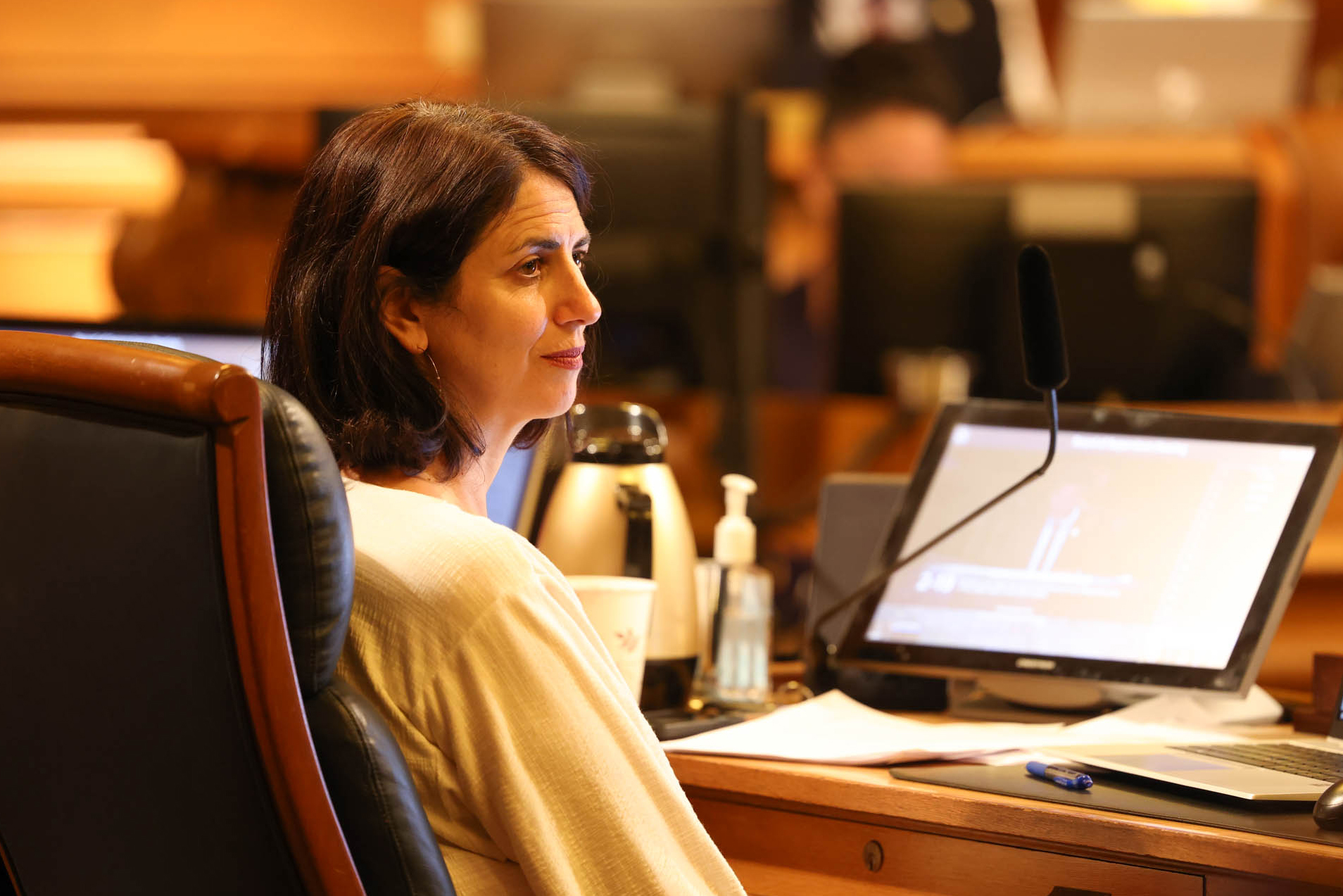 A side profile of a woman in a light sweater sitting in front of a dais with an open laptop. 