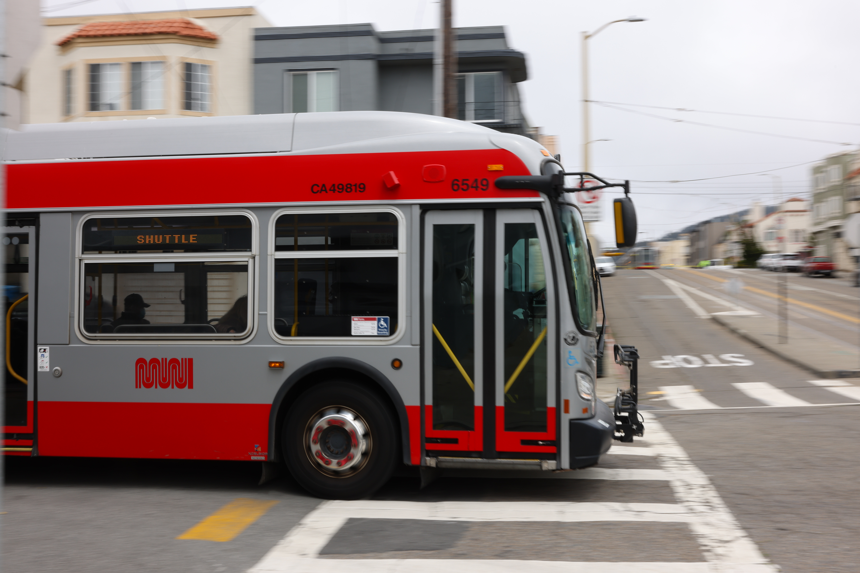 A red and gray city bus, moving on a street with buildings in the background.