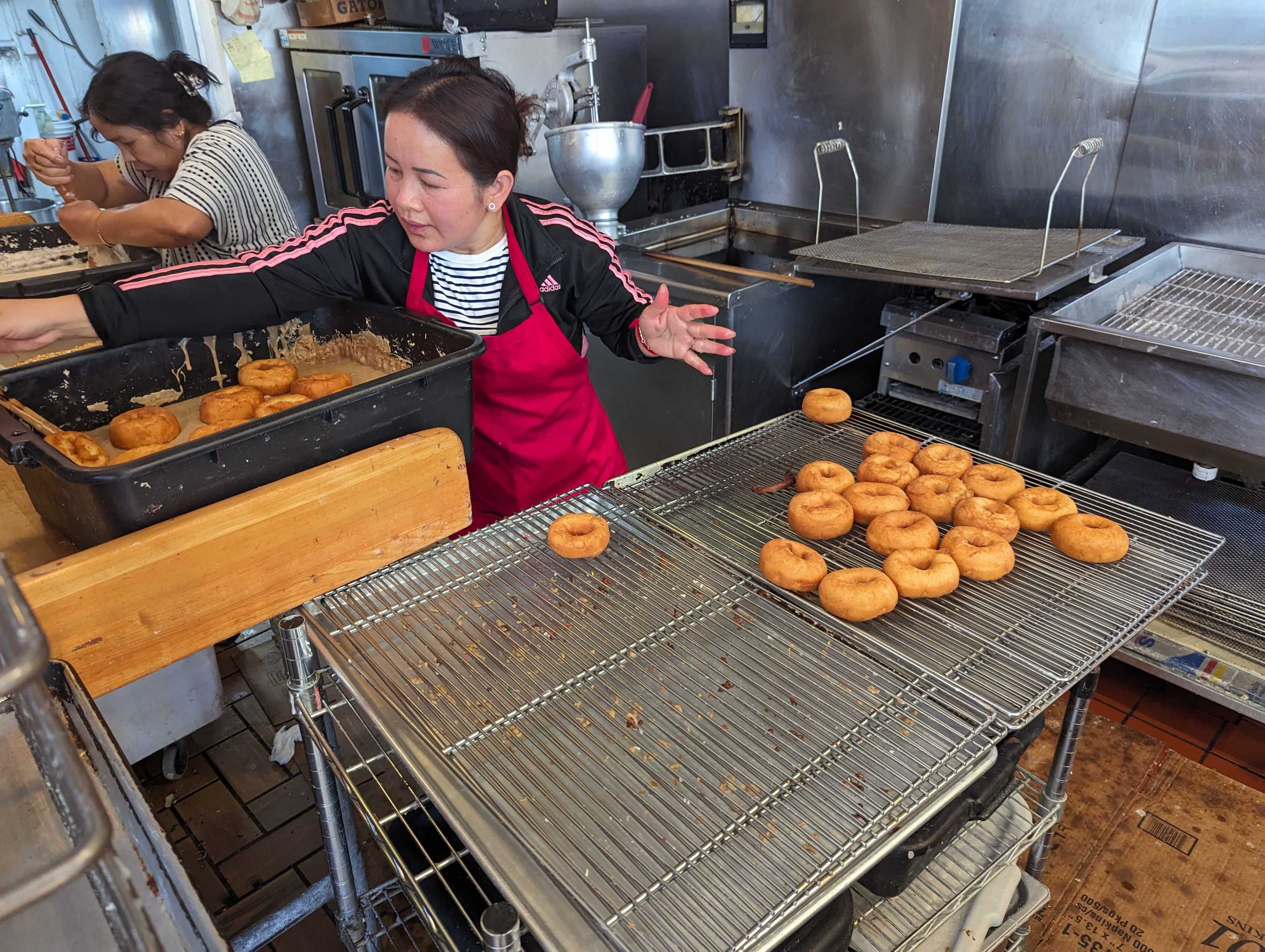 Happy Donuts owner Ratha Vann prepares fresh doughnuts for glazing in her kitchen as a worker readies a batch of batter for cooking.