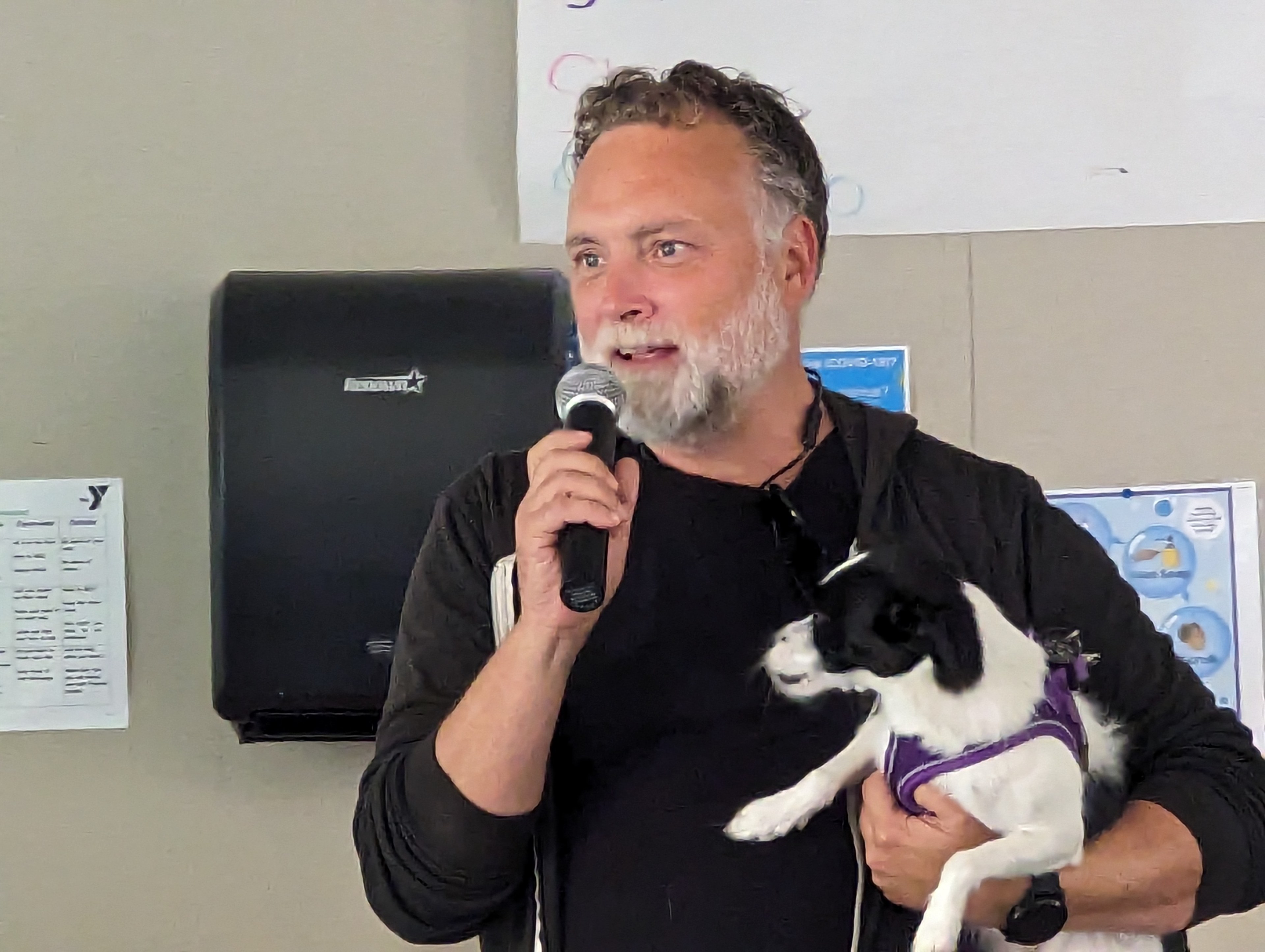 Eric Rozell, director of safe programs for the Tenderloin Community Benefit District, holds a dog named Lady under his arm as he addresses a community gathering at Boeddeker Park's clubhouse in the city's Tenderloin neighborhood Sunday.