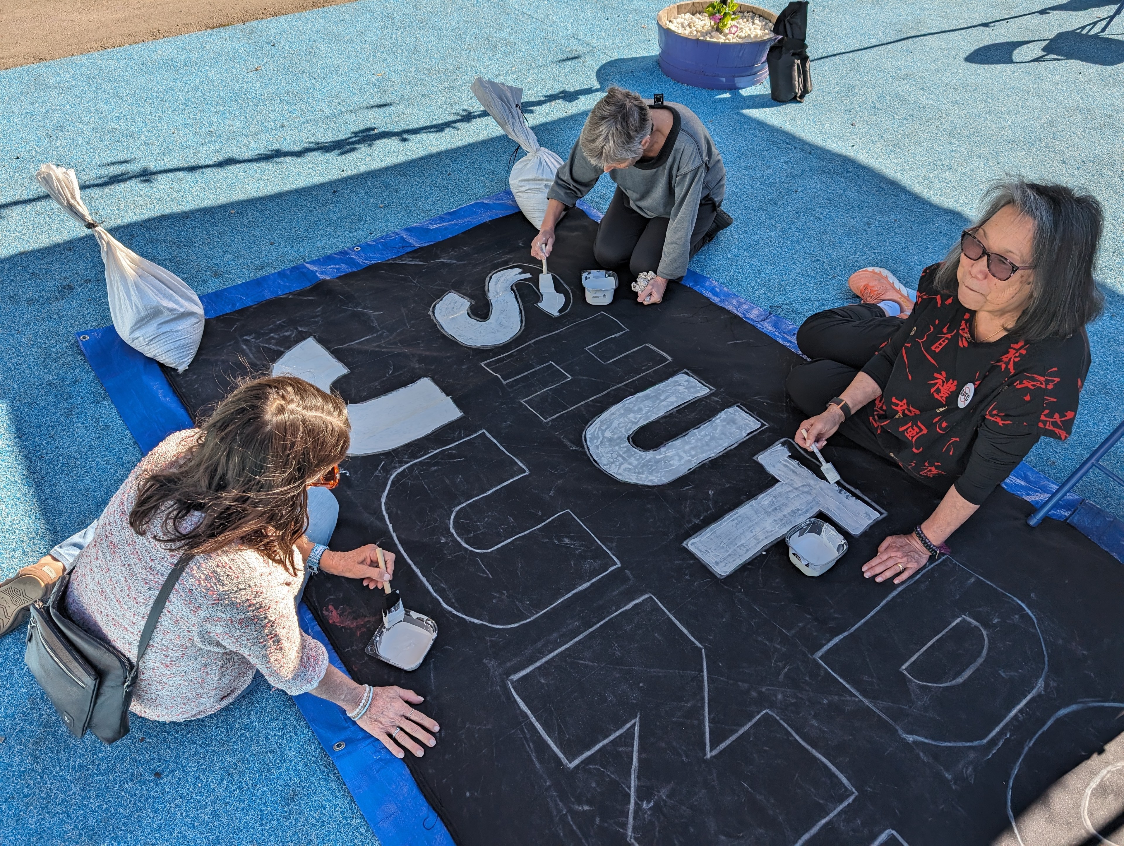 Pam Tau Lee and Kathe Burick paint letters on a “Shut down APEC” sign Sunday at a teach-in at Kawpa Gardens on Mission Street.