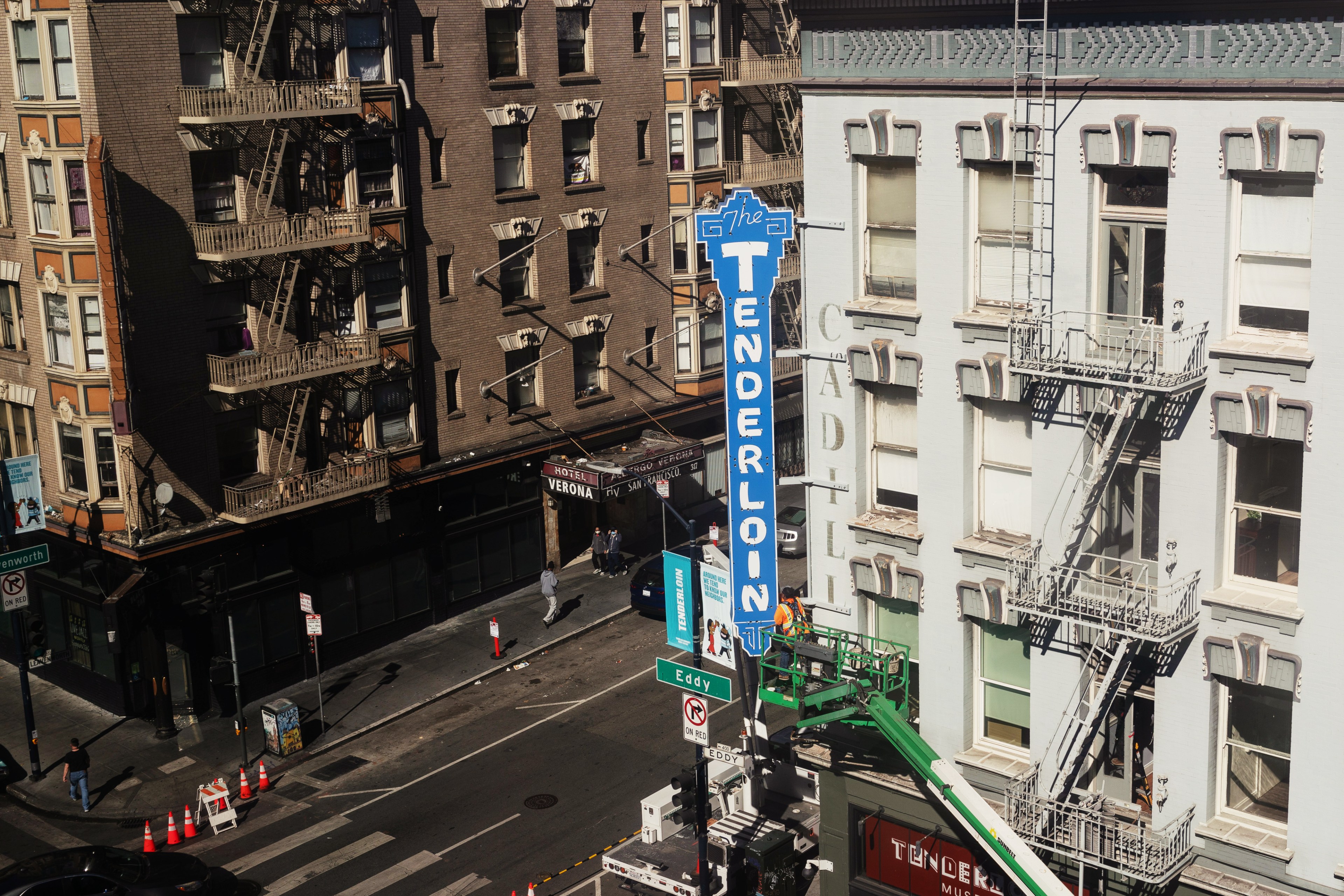 The Hamlin Hotel offers a bird's eye view of The Tenderloin, single-room-occupancy facility in San Francisco. From this vantage point, one can observe pedestrians leisurely walking down the streets, worker repairing the The Tenderloin sign. 