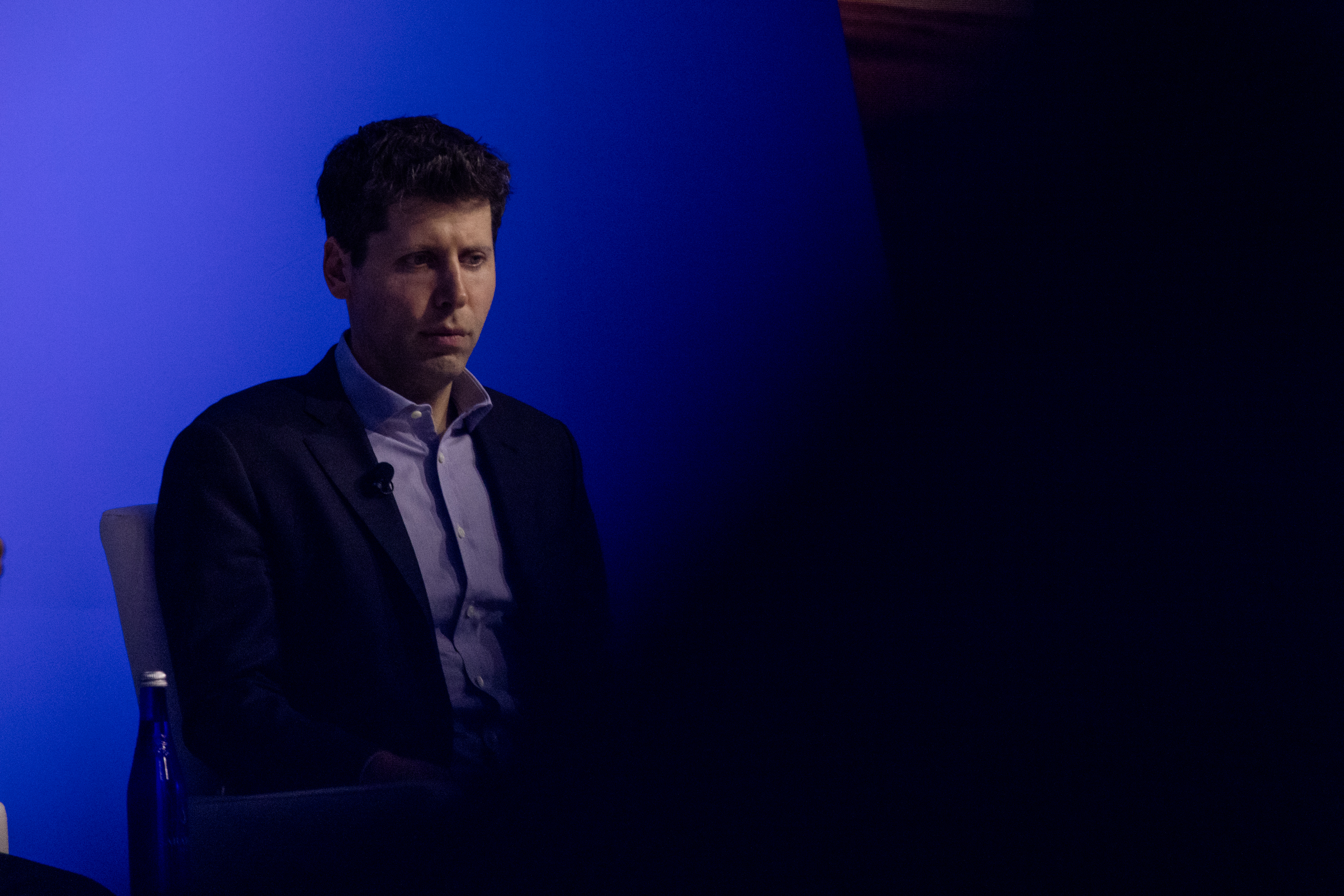 Sam Altman, CEO of OpenAI, looks offscreen with a blue background.