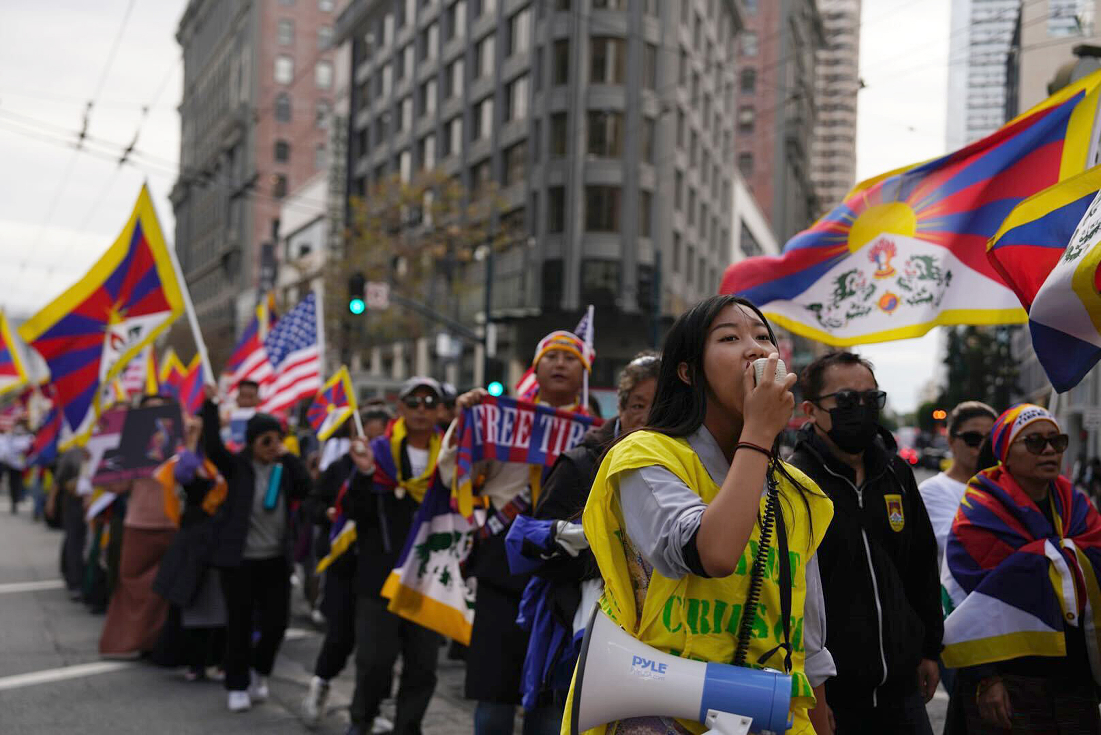 A person screams into a bullhorn during a protest down Market Street. Others in the background hoist Tibetan flags.