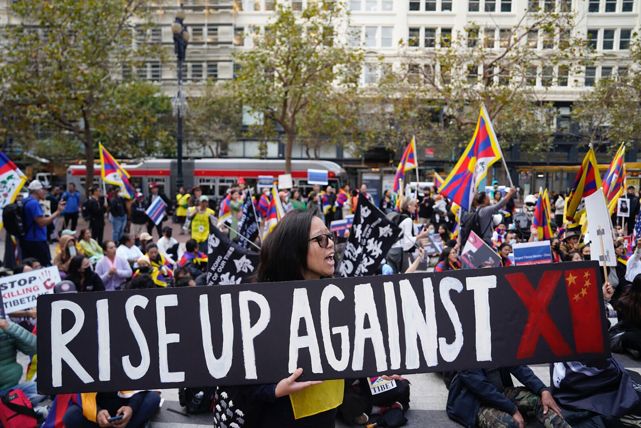 A person holds a sign that reads &quot;Rise Up Against Xi&quot; during a large protest from pro-Tibet demonstrators.