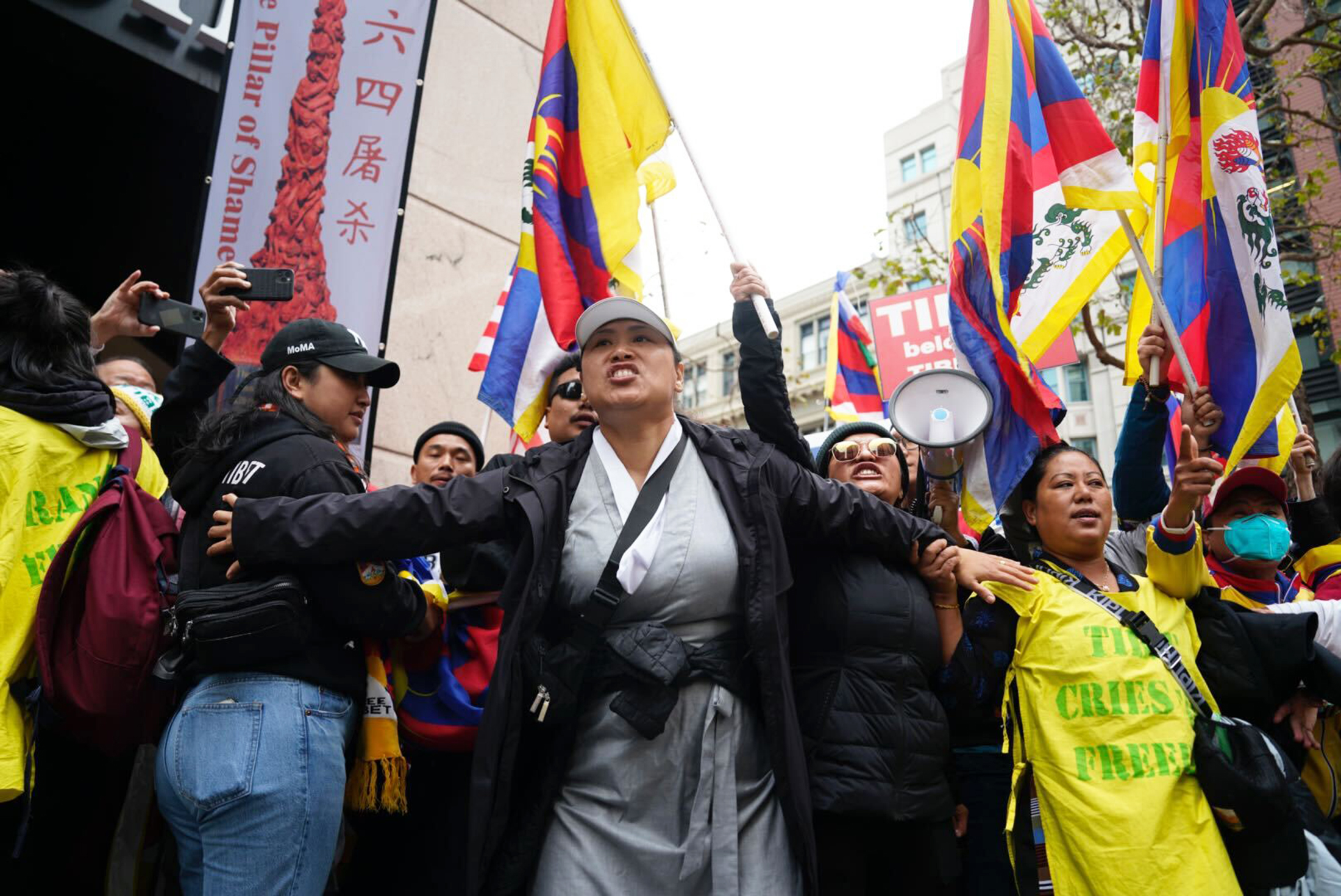 A person screams into into the distance during a protest with Tibetan flags in the background.