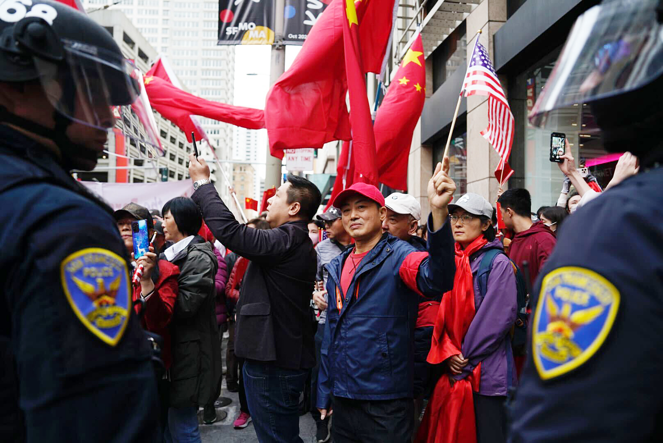 Two San Francisco Police Department officers stand near a rally that includes people waving Chinese flags.