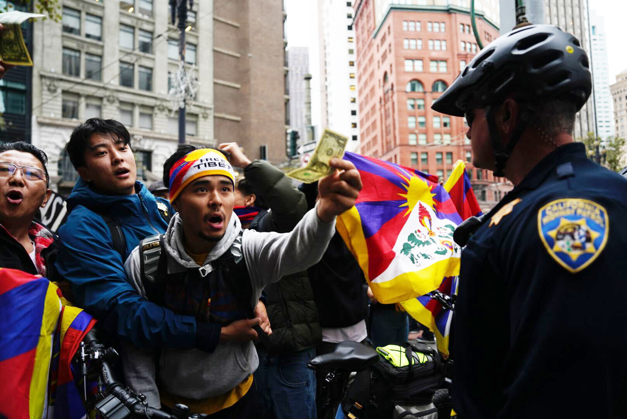 A pro-Tibetan protester points in the direction of pro-China supporters  while holding a US Dollar - SFPD looks on.