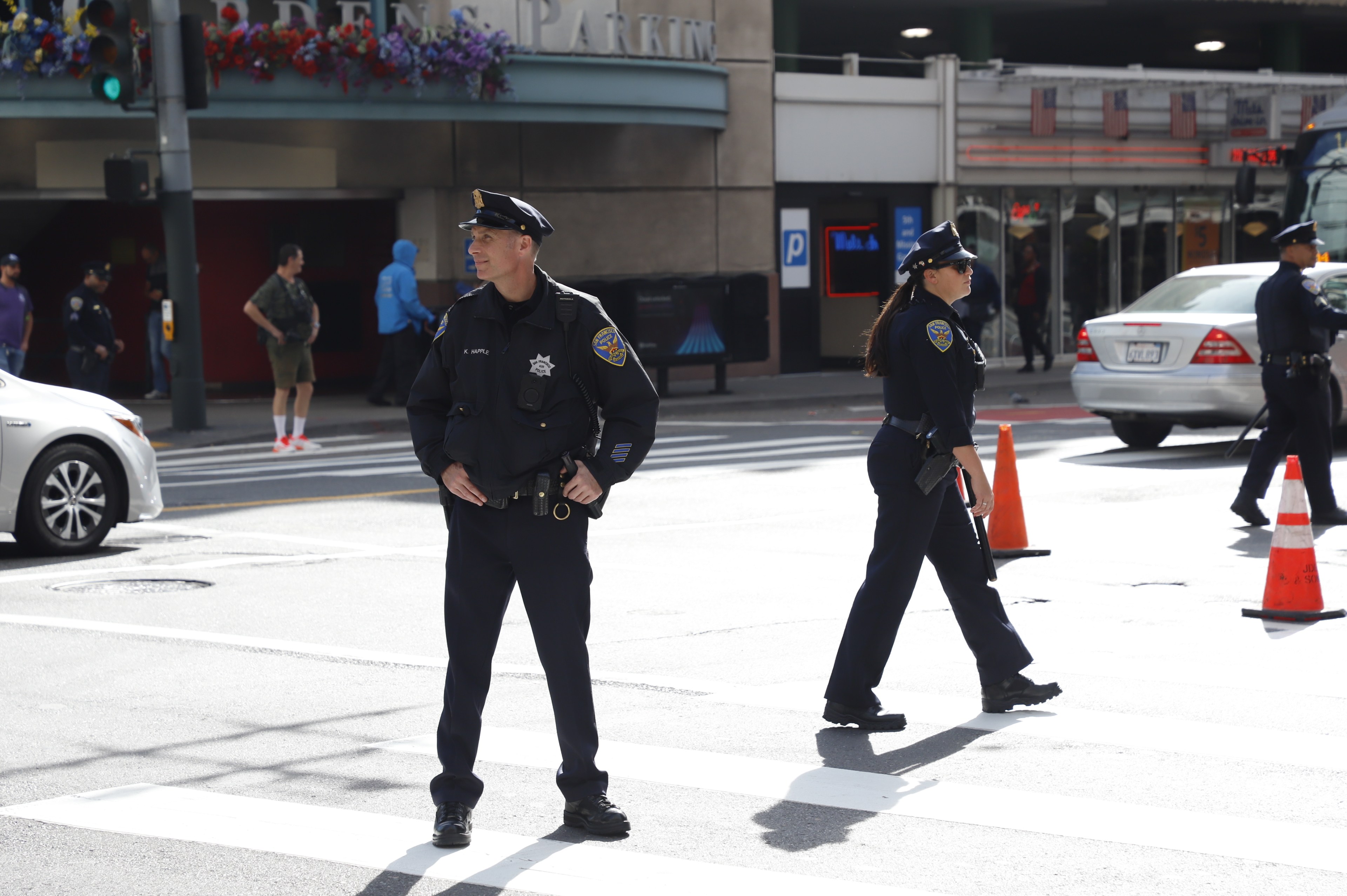 Three SFPD officers stand in the middle of the street forcing traffic to detour behind orange cones.