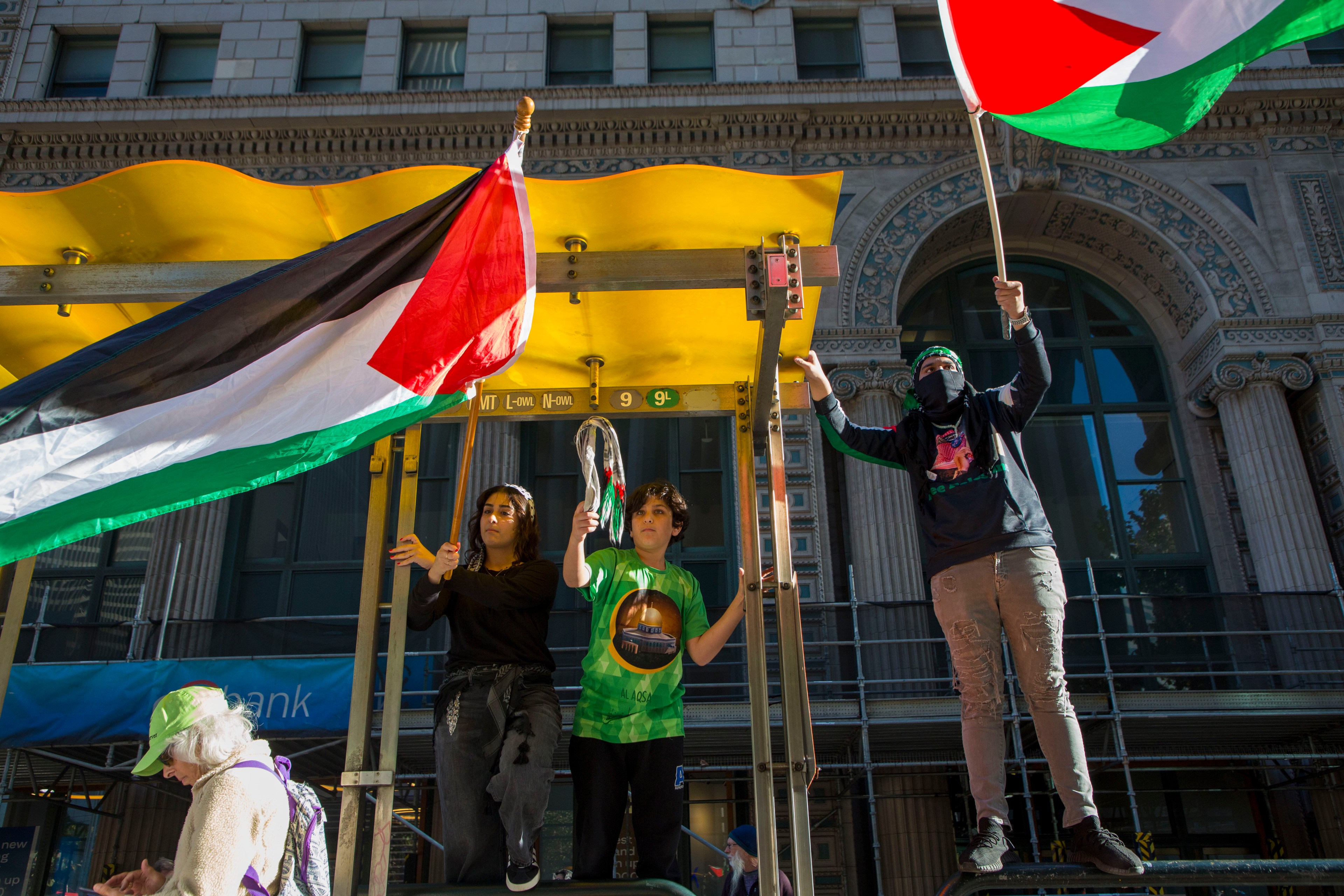 During the No 2 APEC march, three individuals stood atop a bus stop waving the Palestinian flag.