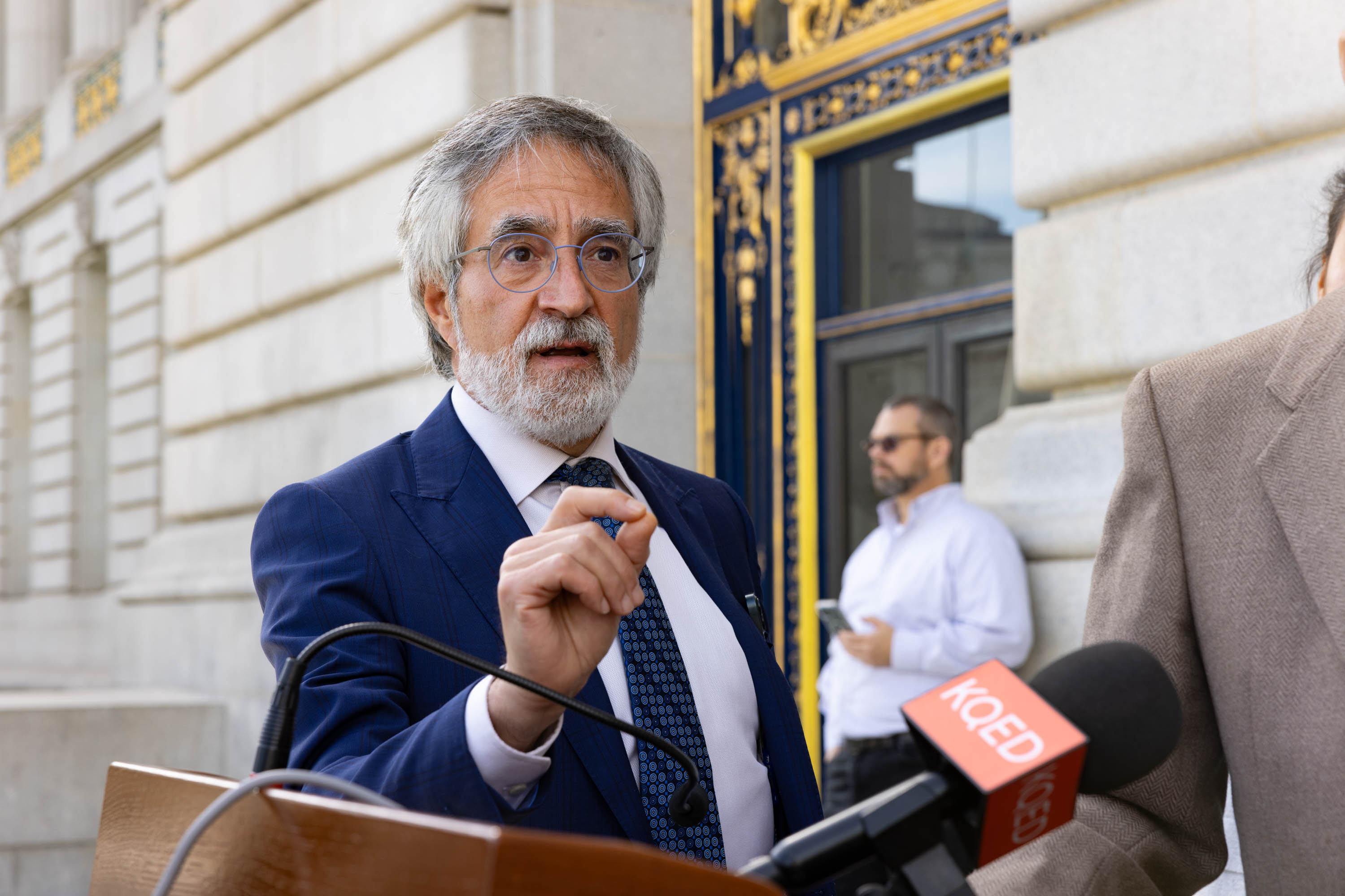 San Francisco Board of Supervisors President Aaron Peskin, in a blue jacket, answers a reporter's question outside city hall in San Francisco.