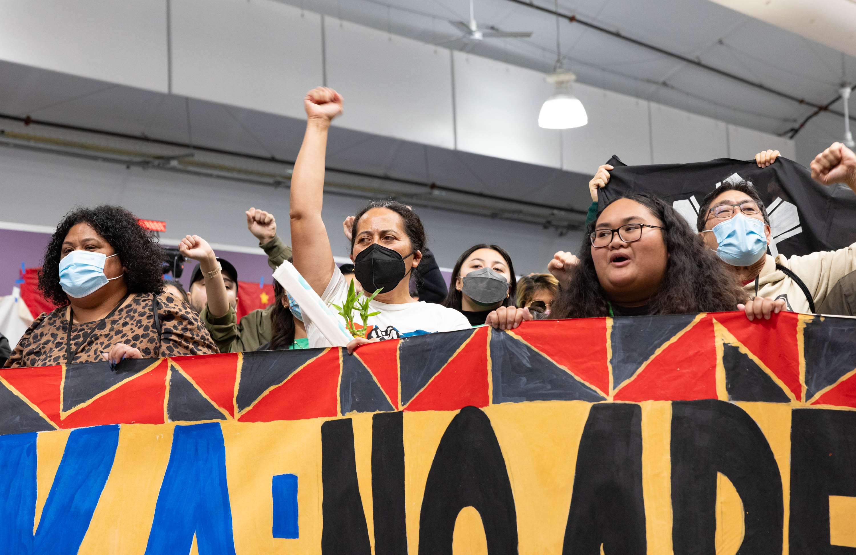 Several people stand behind a banner with their fist raised.