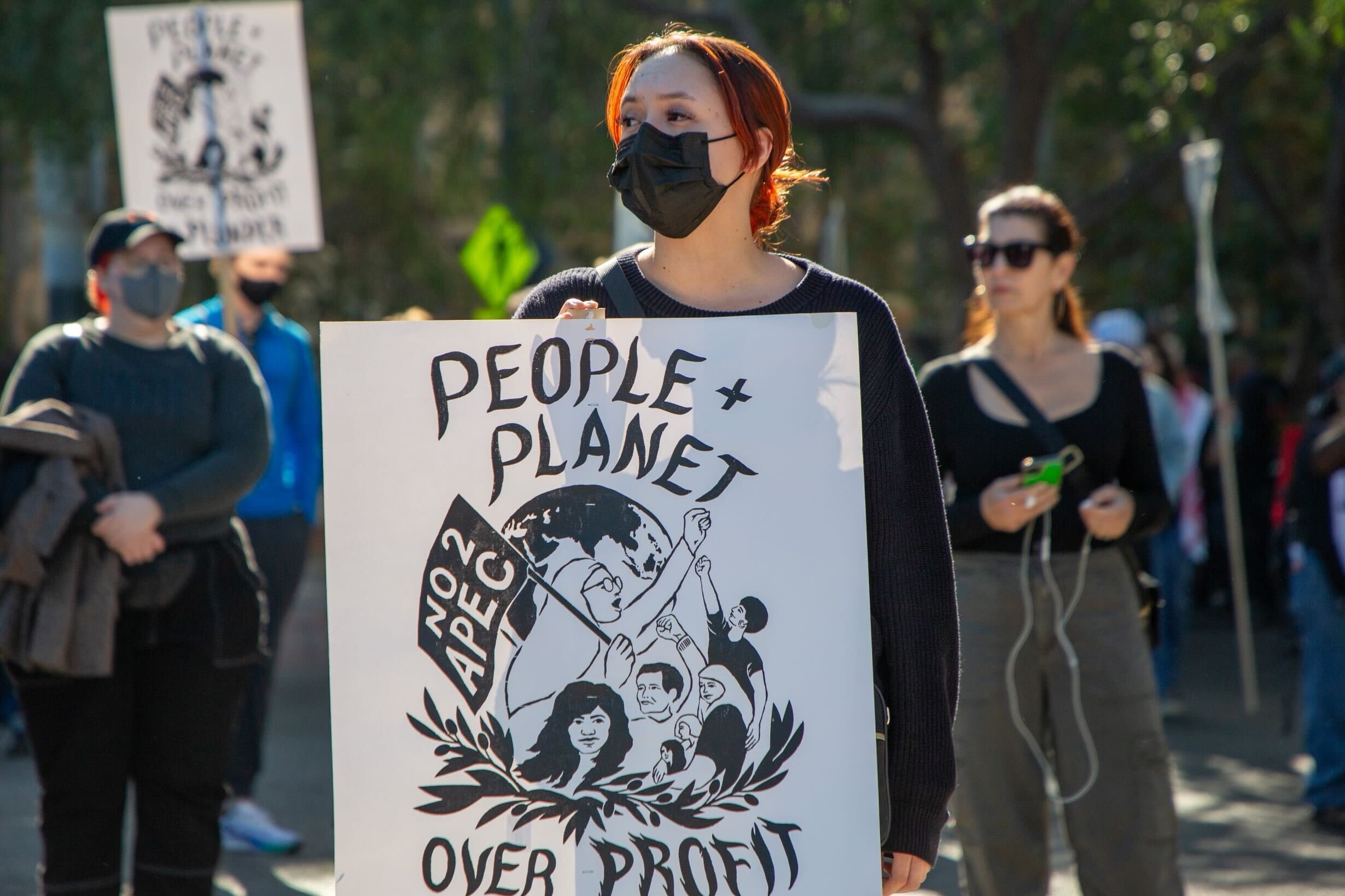 A woman holds a sign that reads “People + Planet over Profit + Plunder” during a “No to APEC” protest in San Francisco.