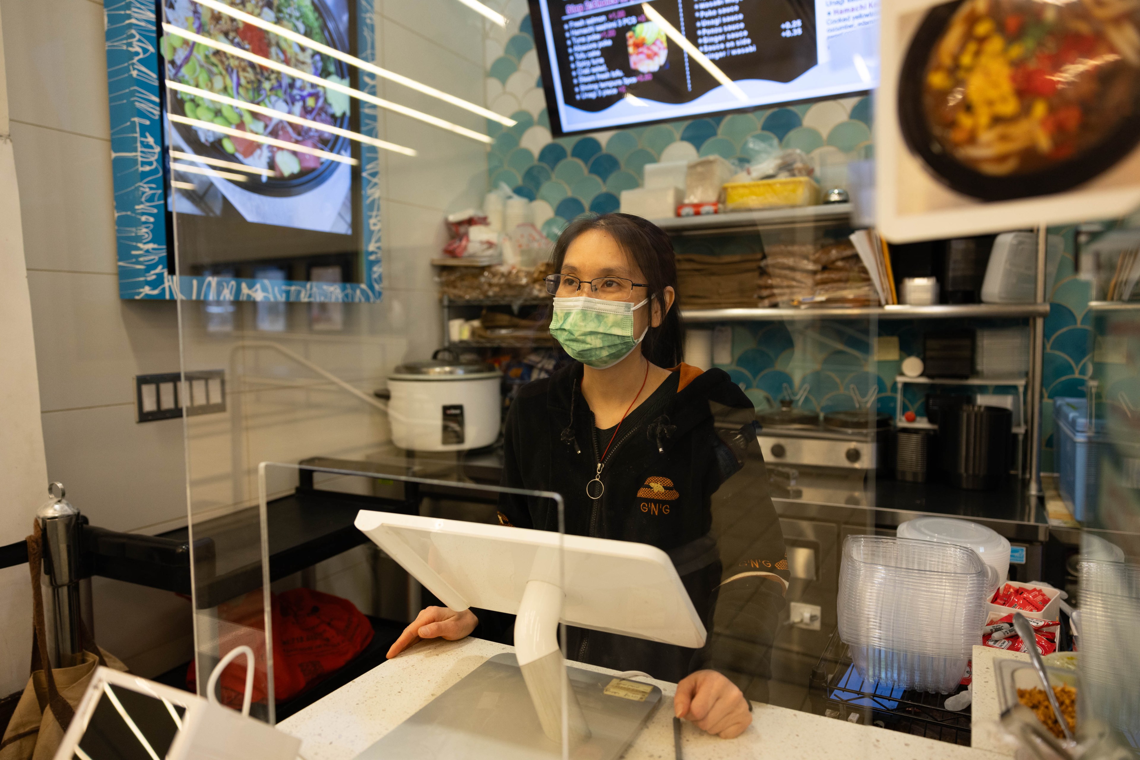 A woman stands behind a cash register at a restaurant counter.