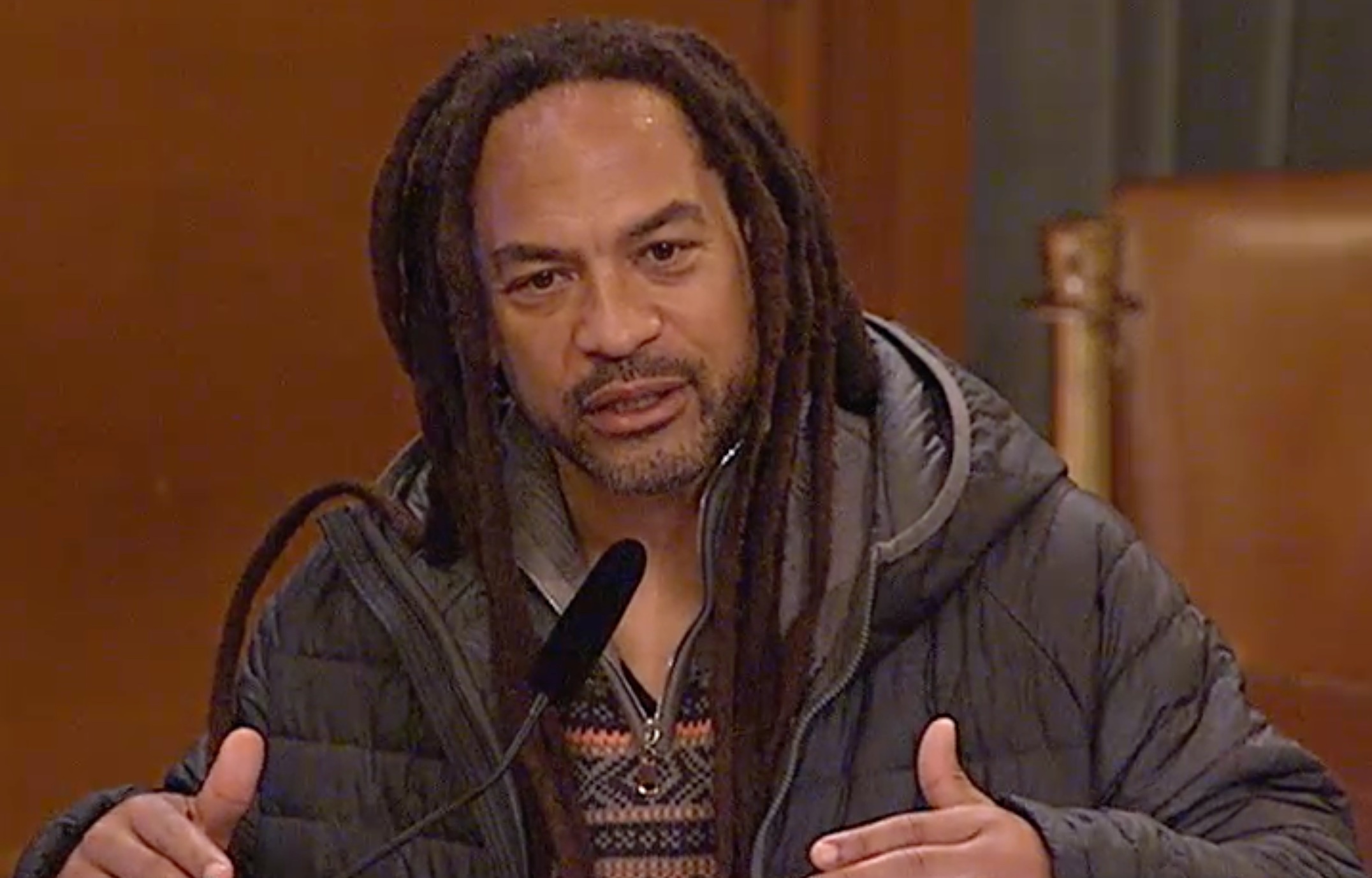A man with dreadlocks speaks into a microphone.