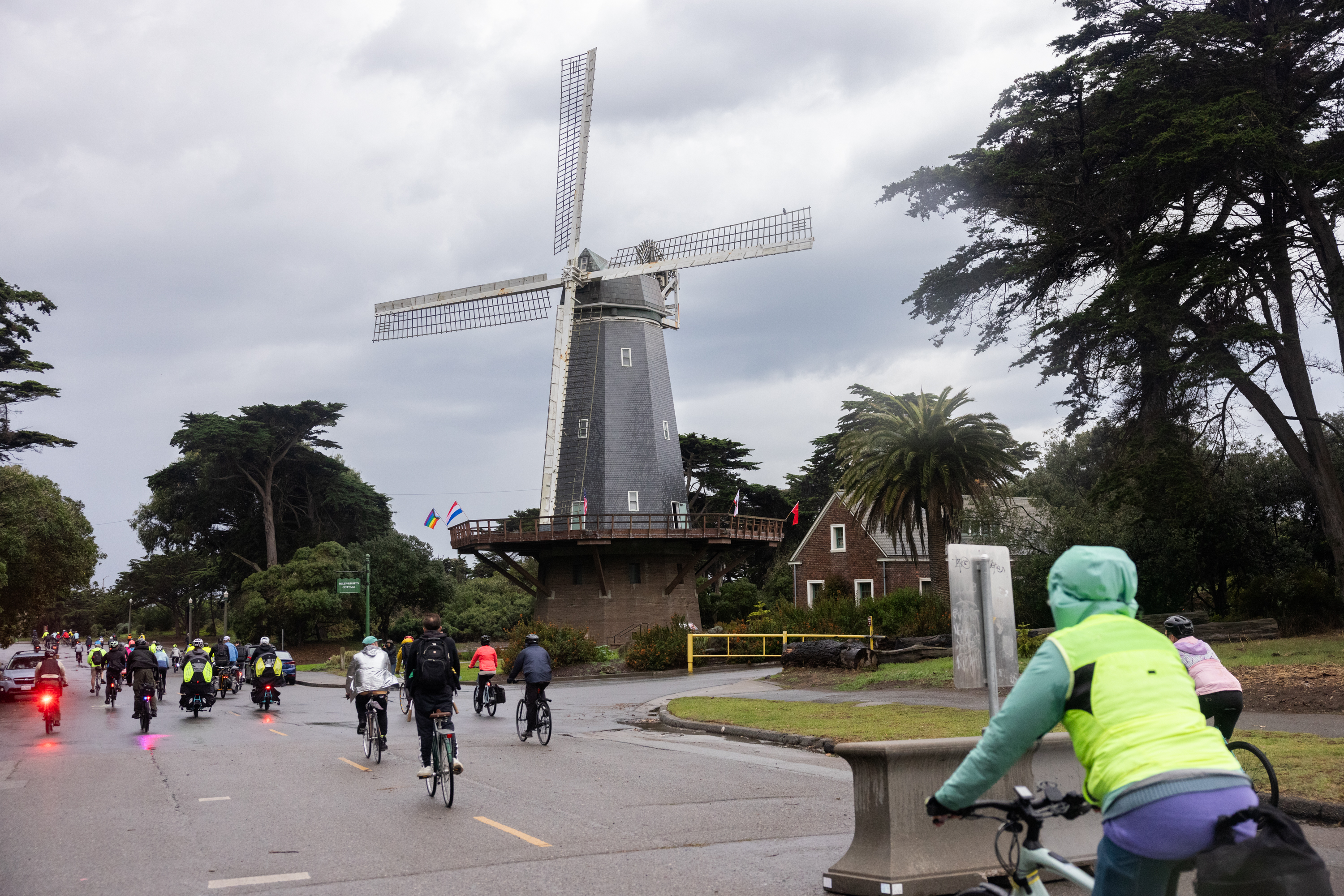 A group of people on bikes pass by Queen Wihelmina Garden in the rain.