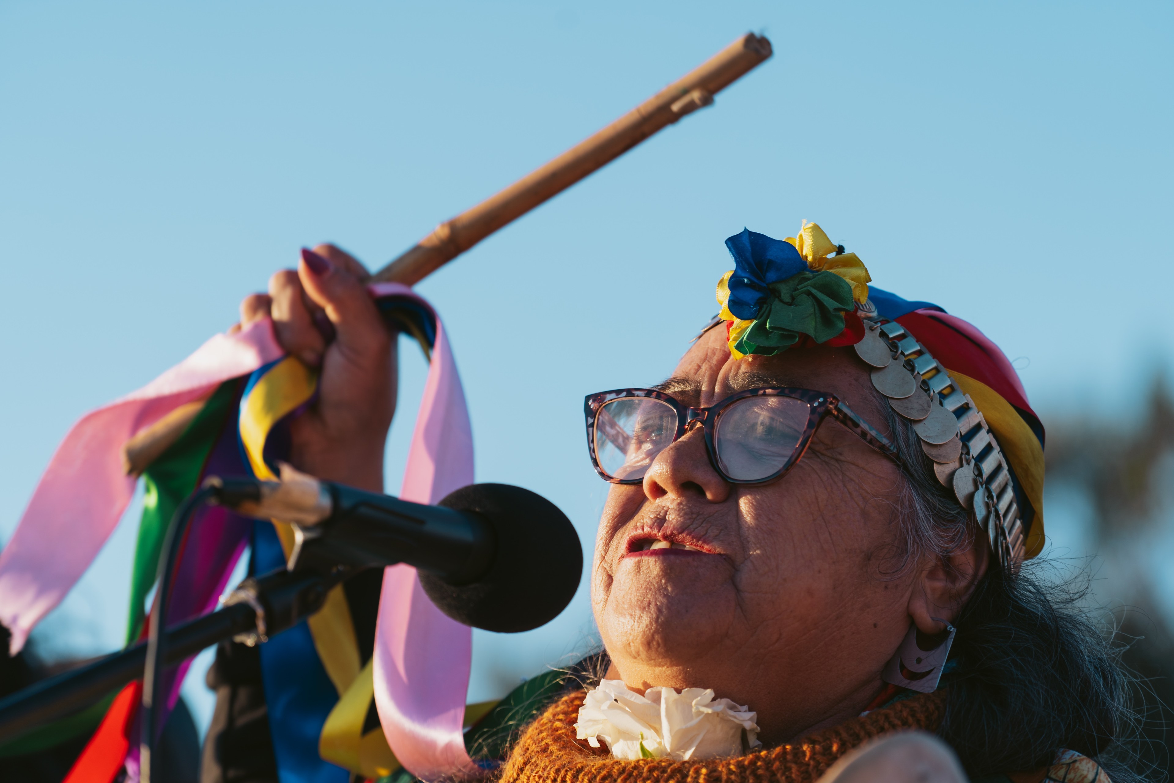 A close-up of a person wearing a colorful scarf headdress and holding a flute in one fist.