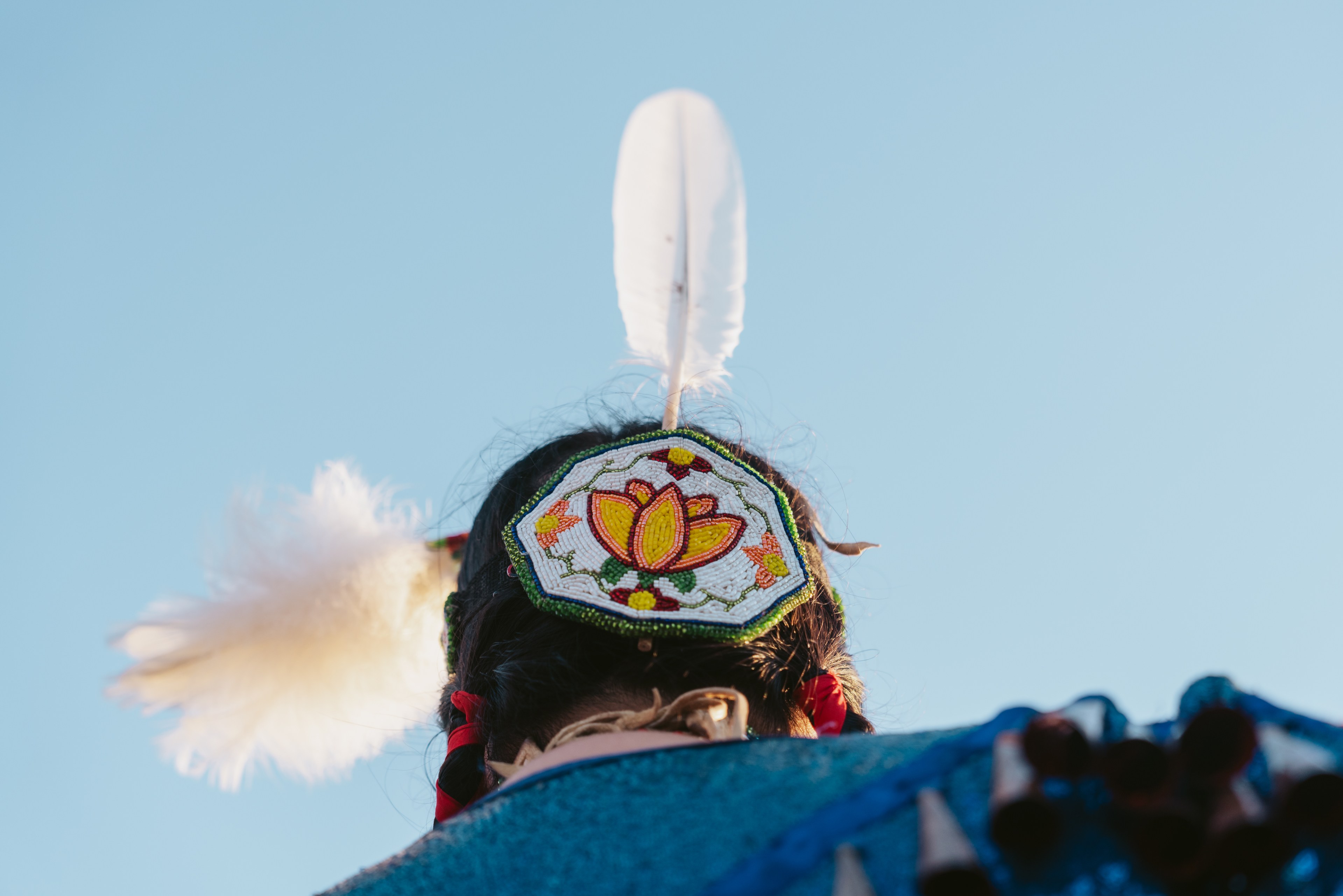An image of a person's head adorned by a beaded headdress with white feathers.