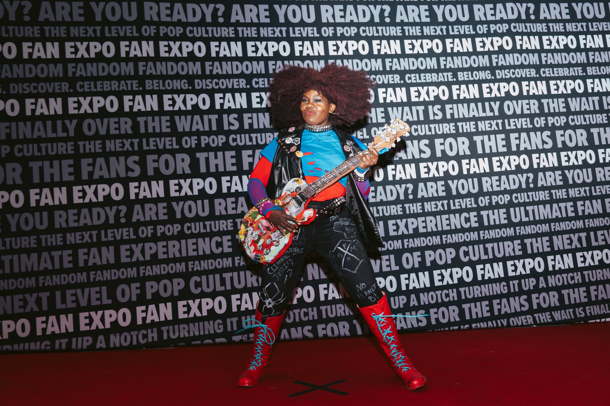 A woman holds a guitar in front of a step-and-repeat.