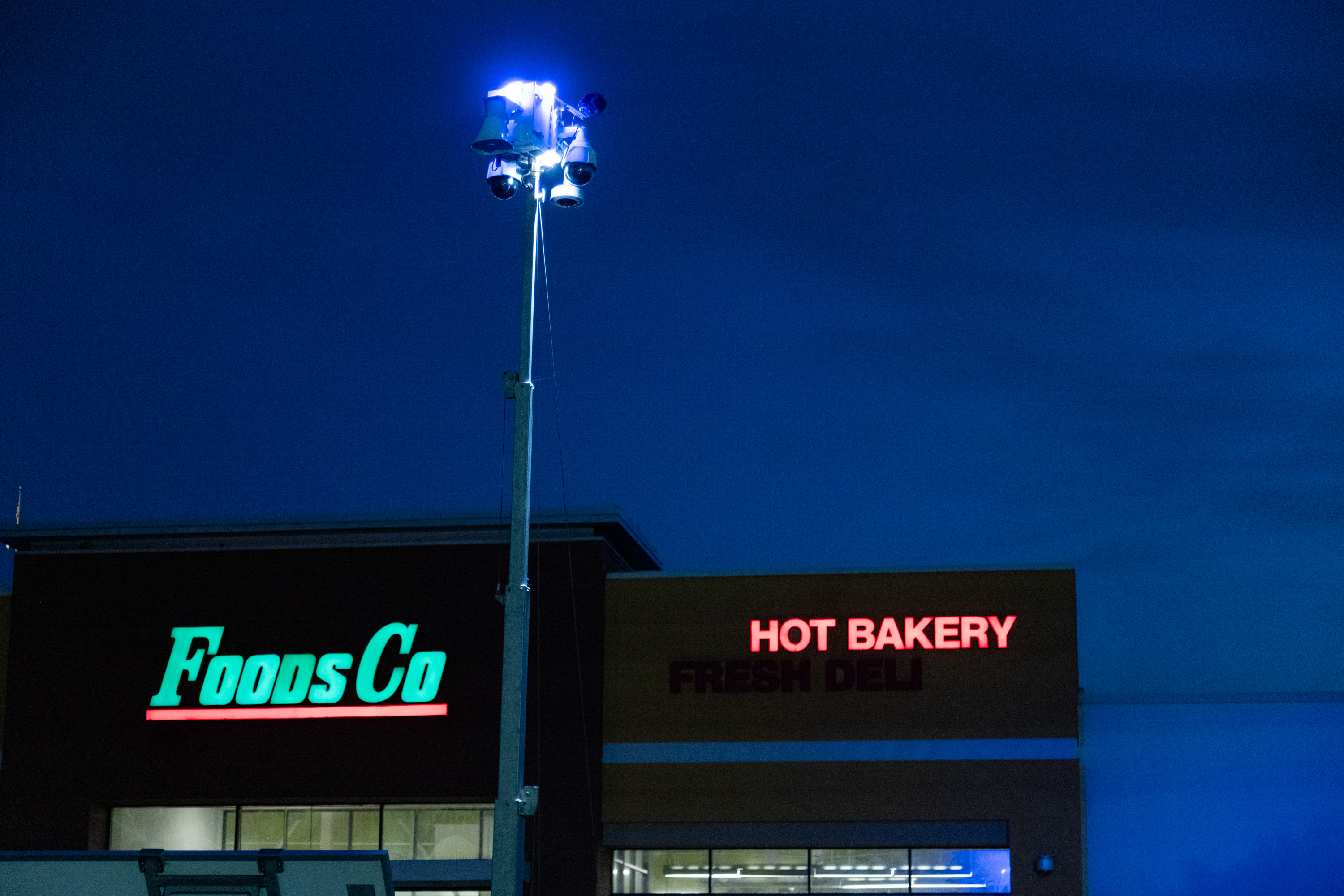 A security camera is set up in a parking lot of a Foods and Co at night.