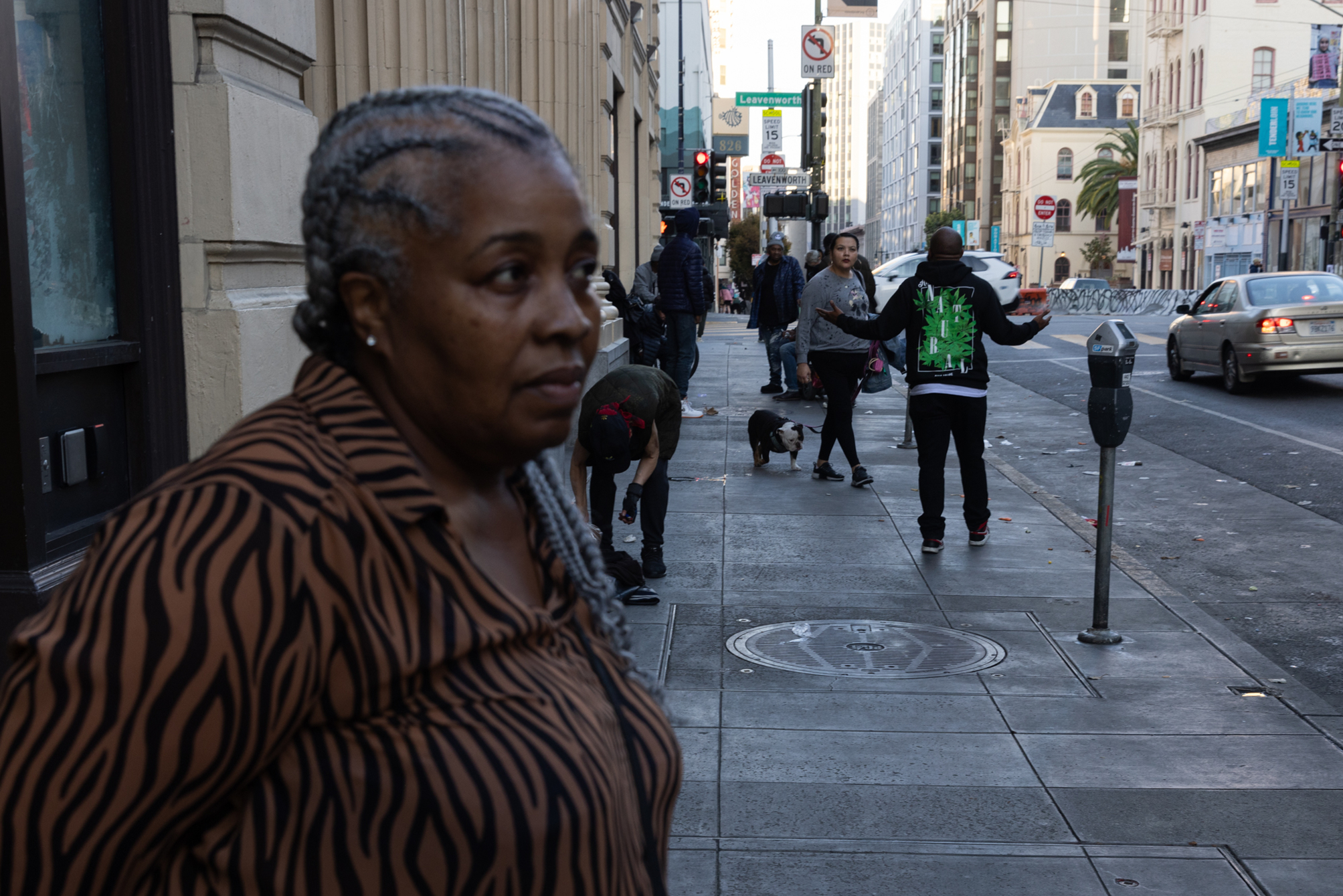 Cheryl Thornton stands on the sidewalk facing off camera with pedestrians congregating behind her outside of her place of work in San Francisco. 