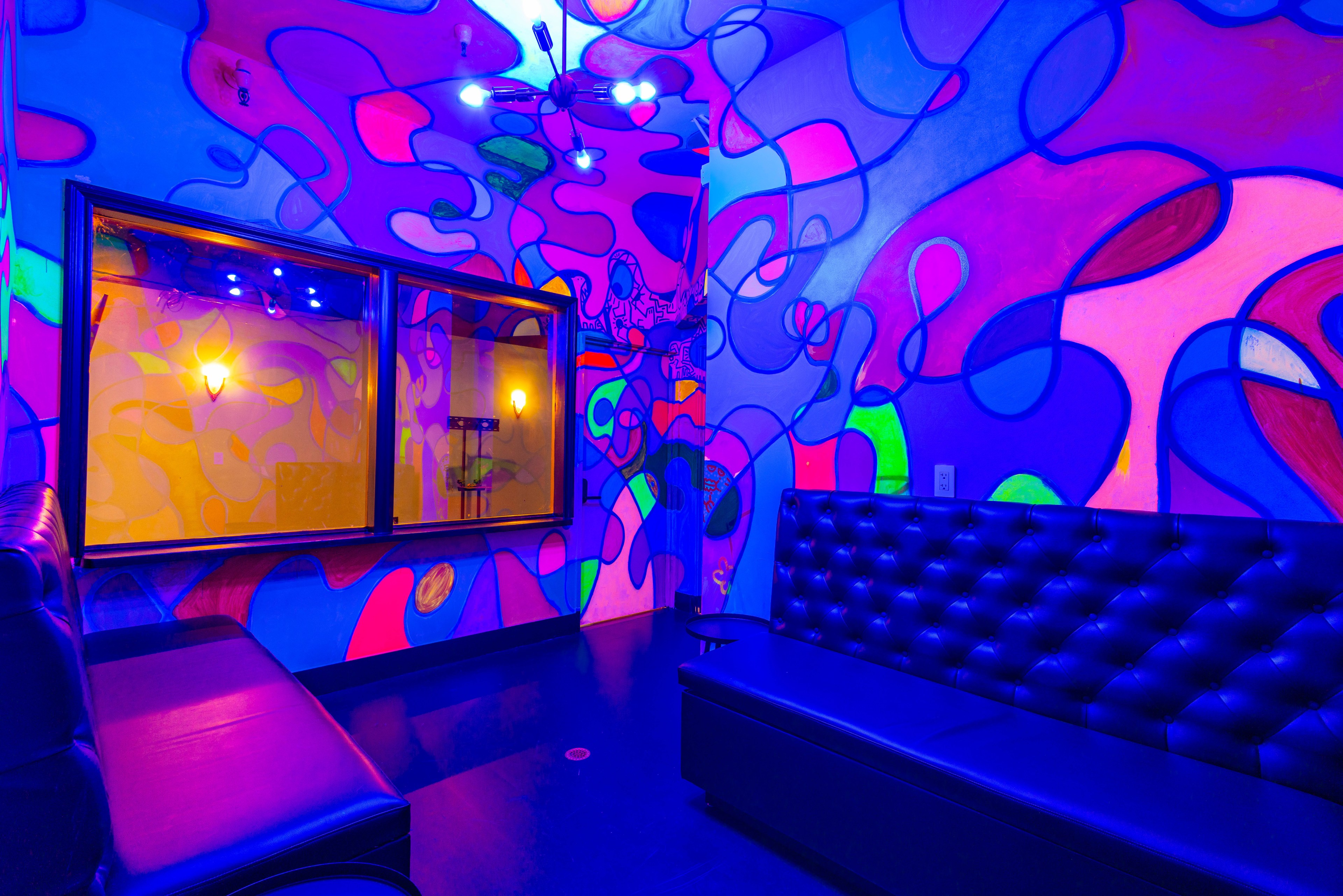 A blacklit mural glows in bright shades of color within a windowed room with a low banquette and couch