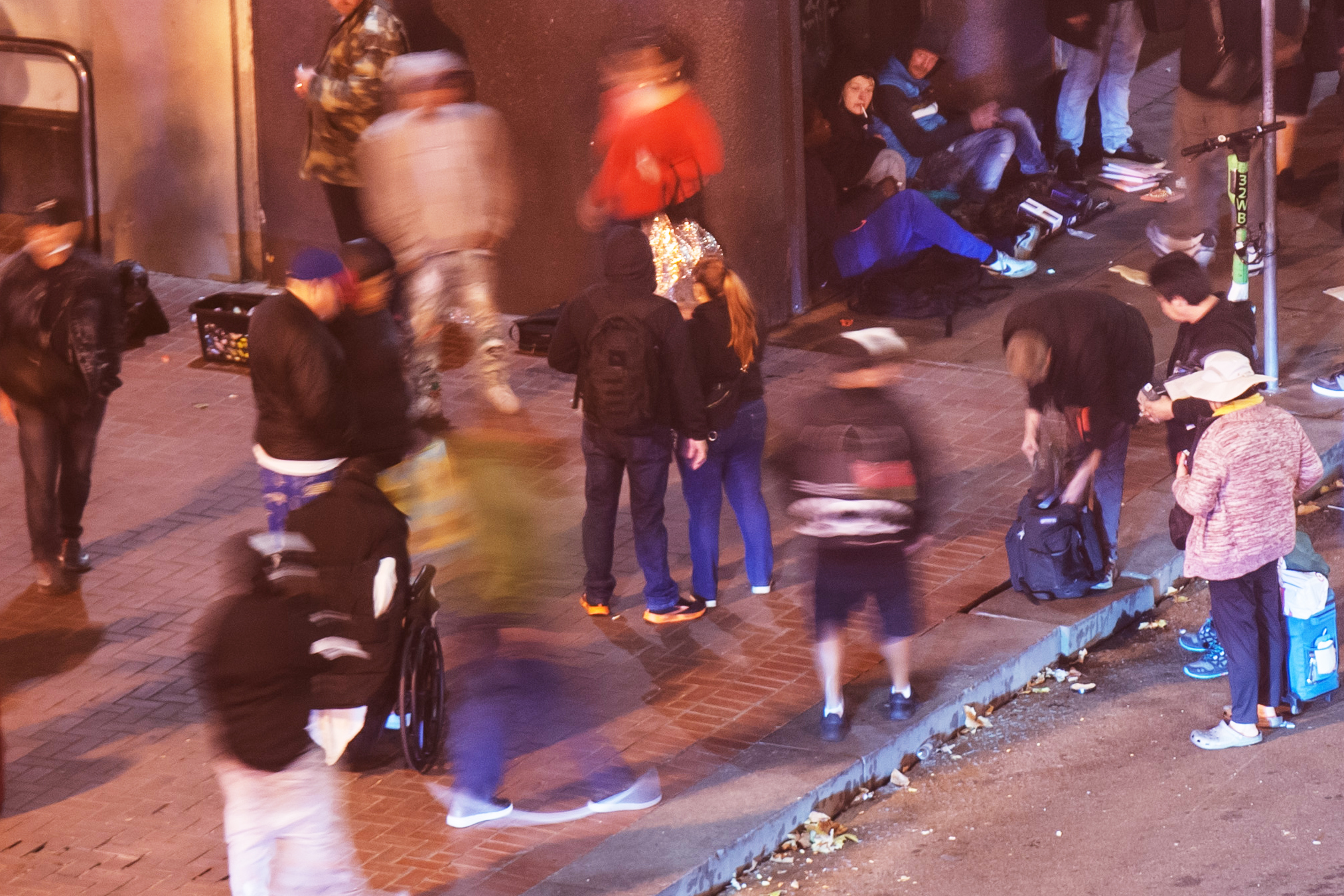 A street scene of blurry figures at night in downtown San Francisco. The area is know for drugs and homelessness.