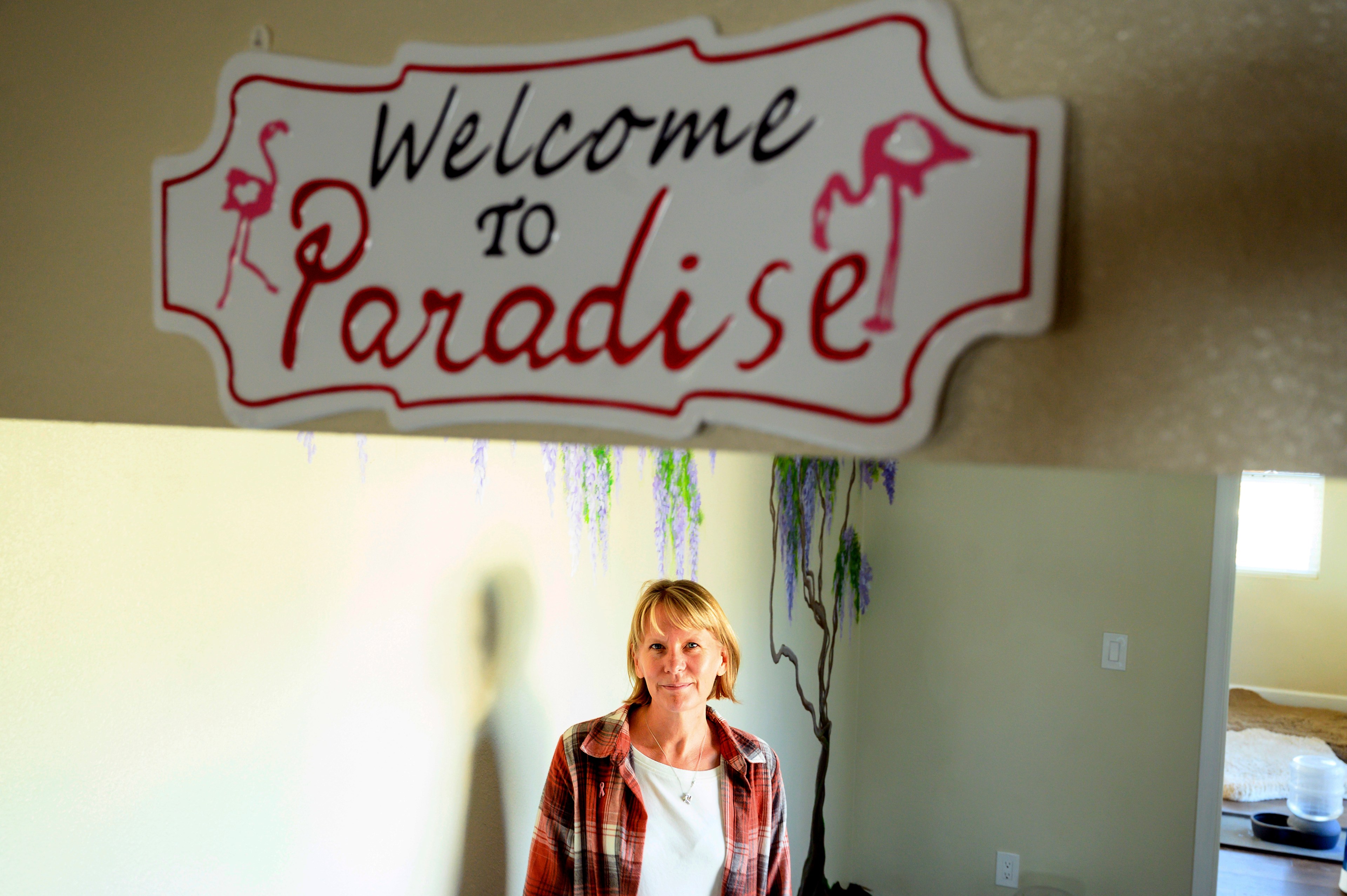 Woman stands in front of a sign saying "Welcome to Paradise"