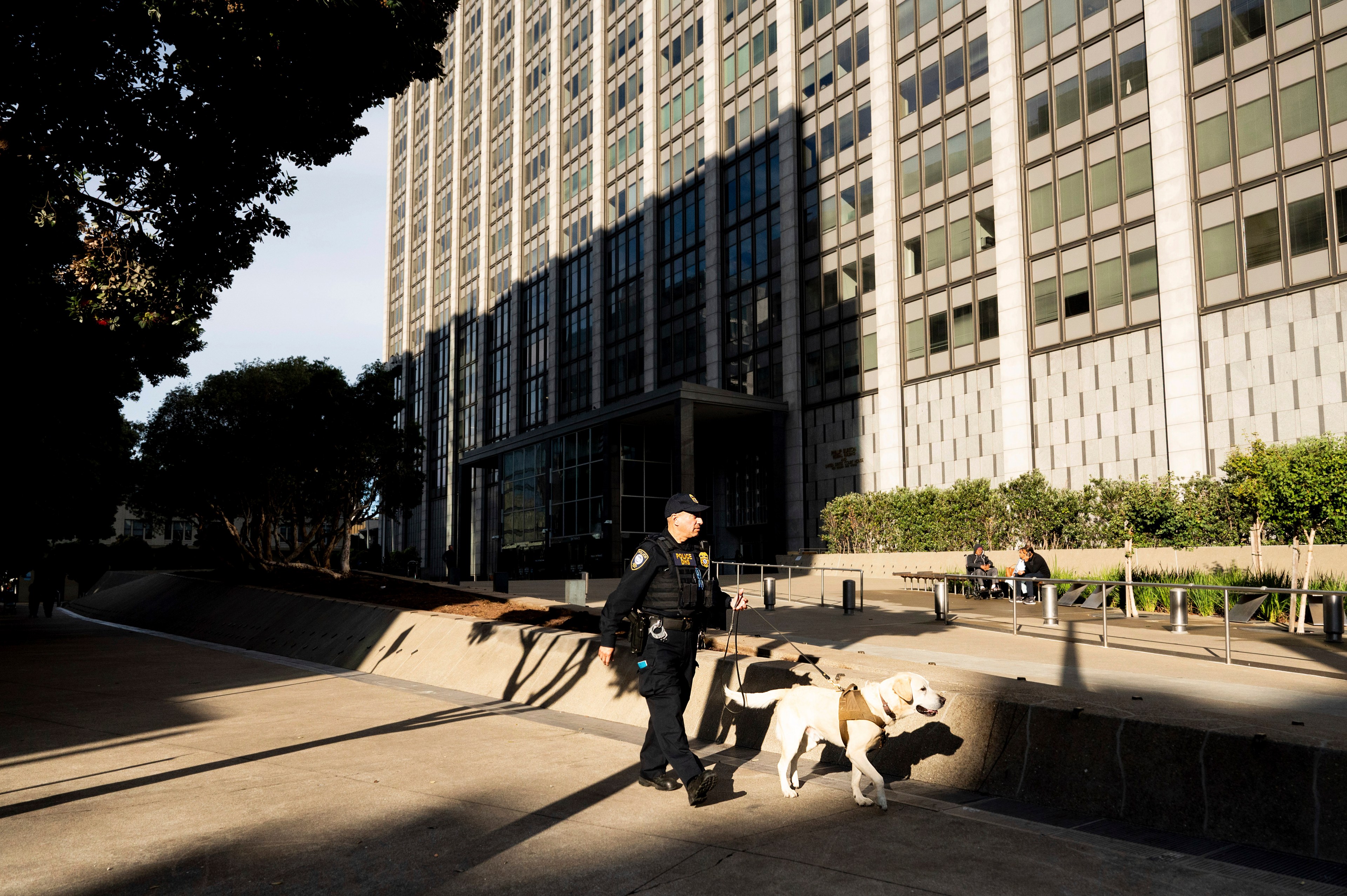 A police officer walks around the exterior a federal building with a dog.