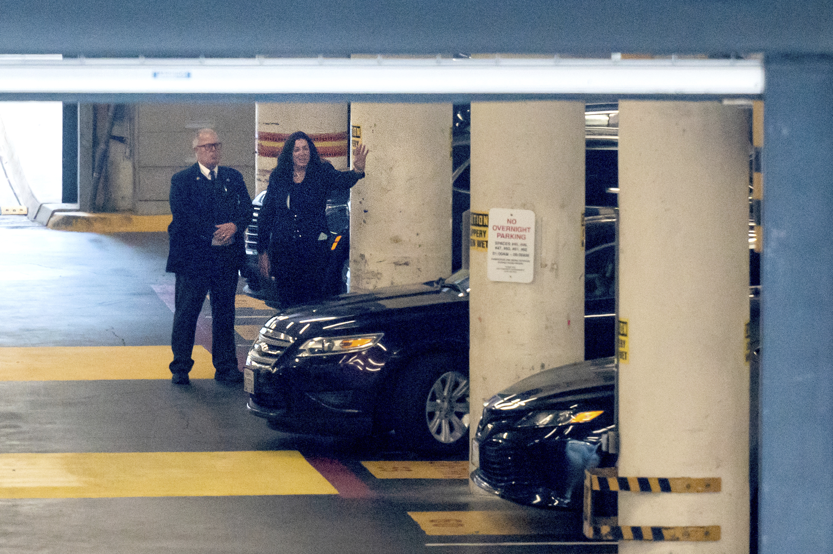 Christine Pelosi walks by two cars in a parking garage beside a man.