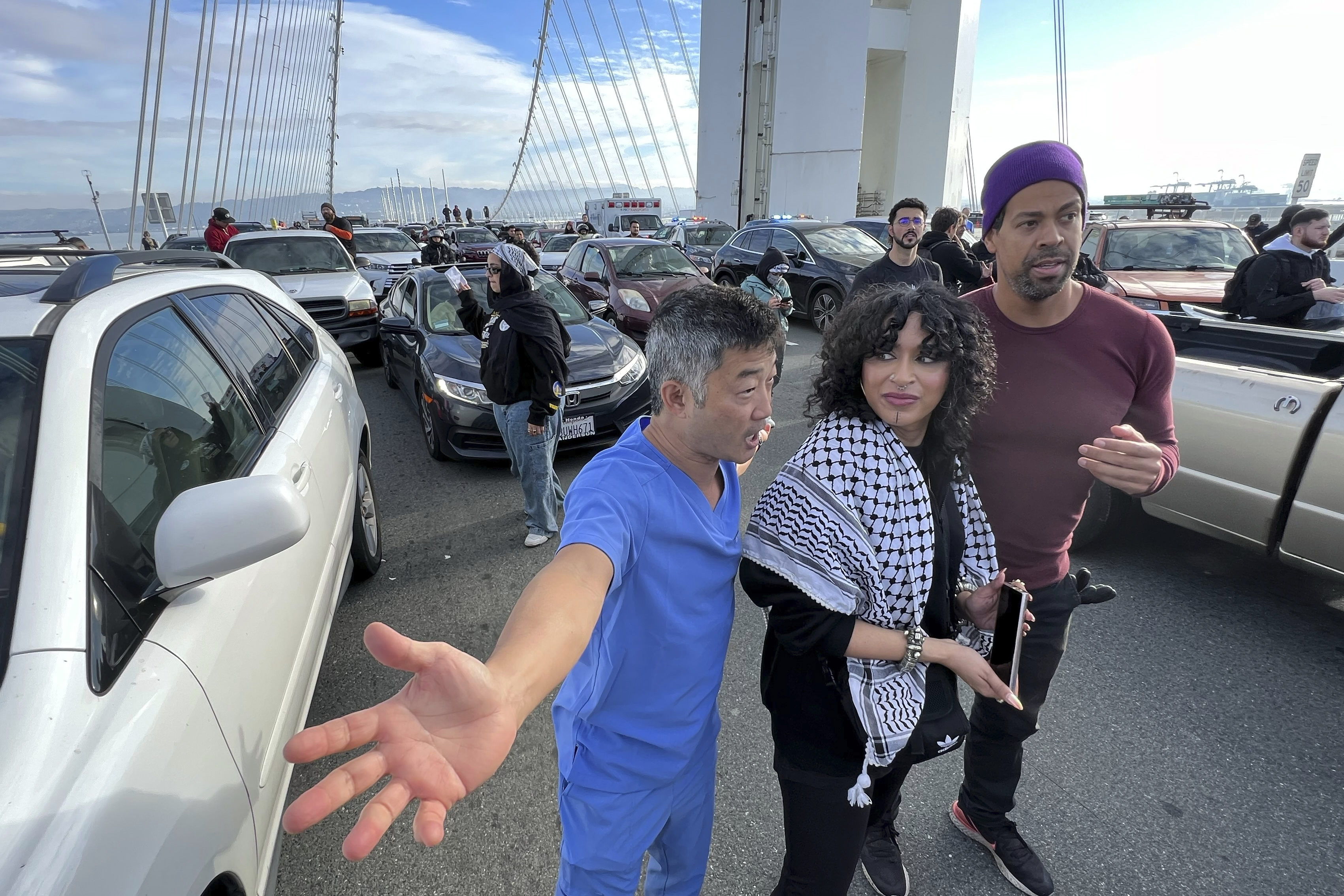 An exasperated person with their arms spread, yelling in the direction of 2 protesters stands between gridlock traffic during a protest on the Bay Bridge.