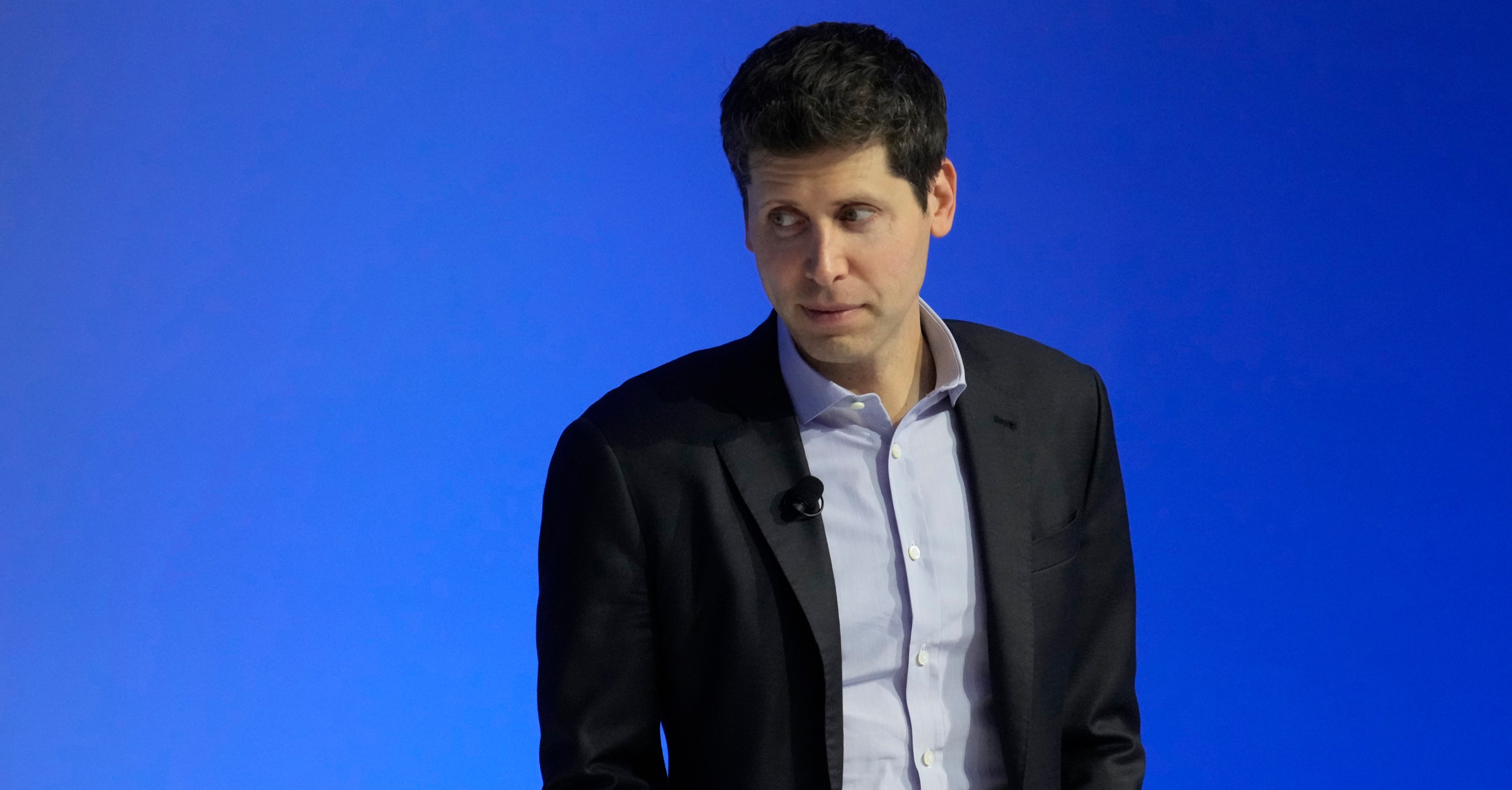 Sam Altman, CEO of OpenAI looks offscreen with a blue background.