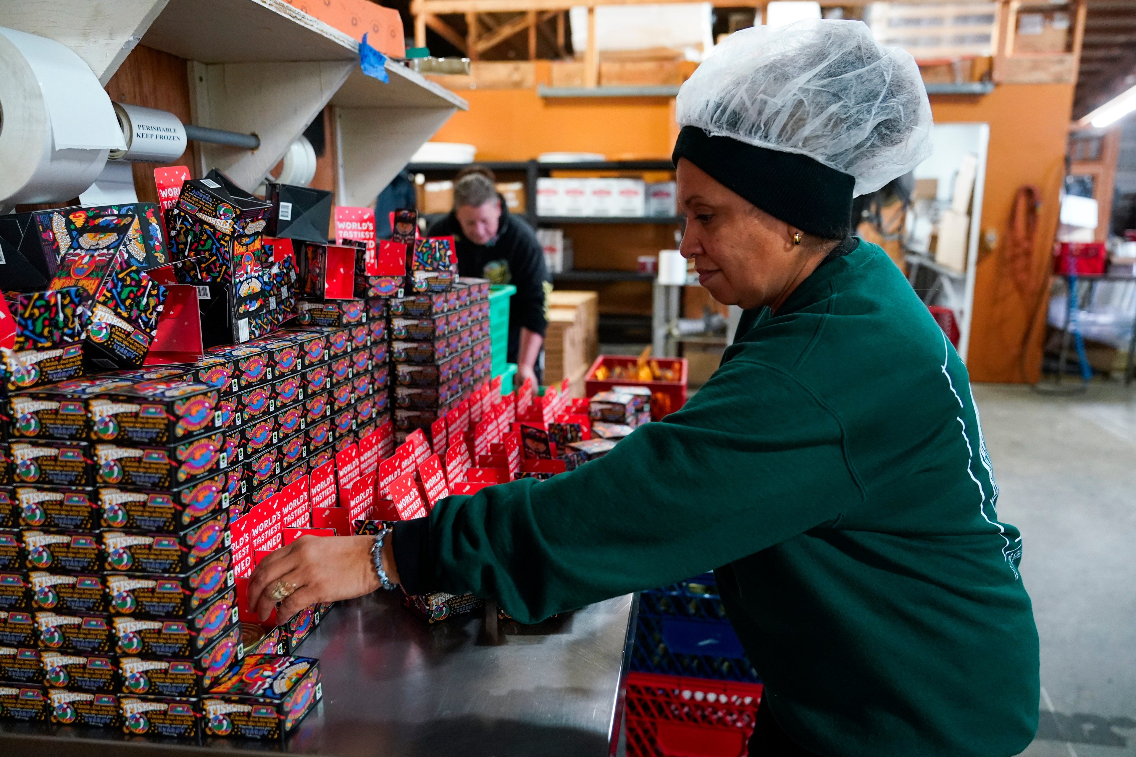 A factory worker with a row of tinned fish items being packaged.
