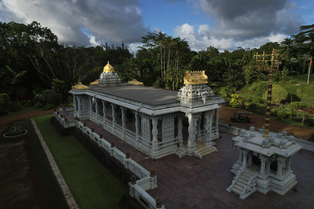 A white temple made of granite and topped with gold decorations sits in a tropical clearing.