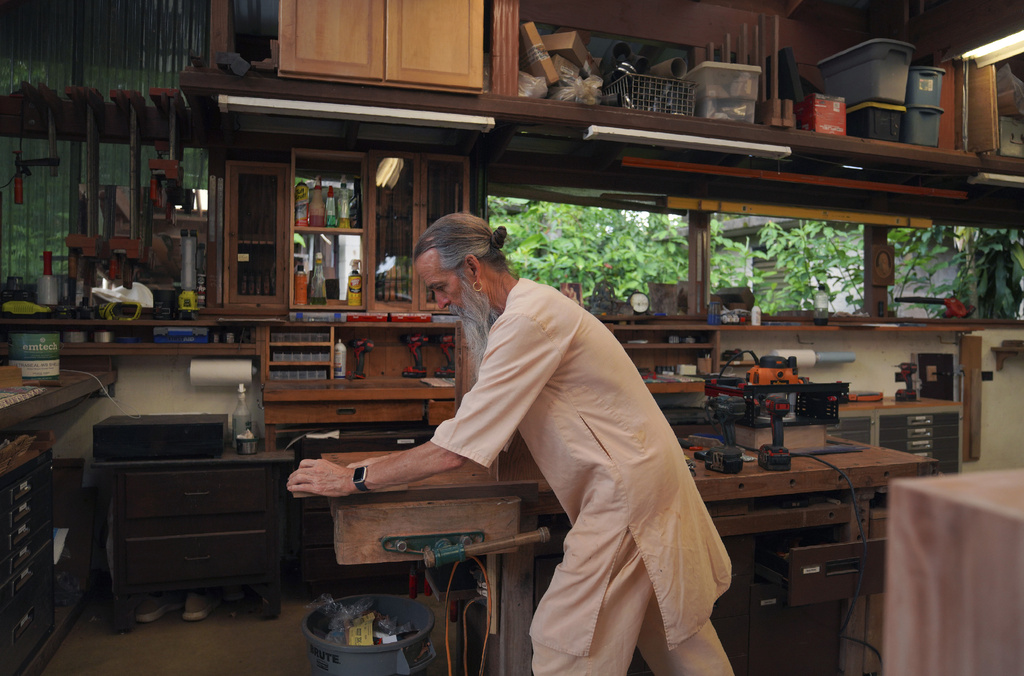 A man in a white top and pants works in a woodworking shop.