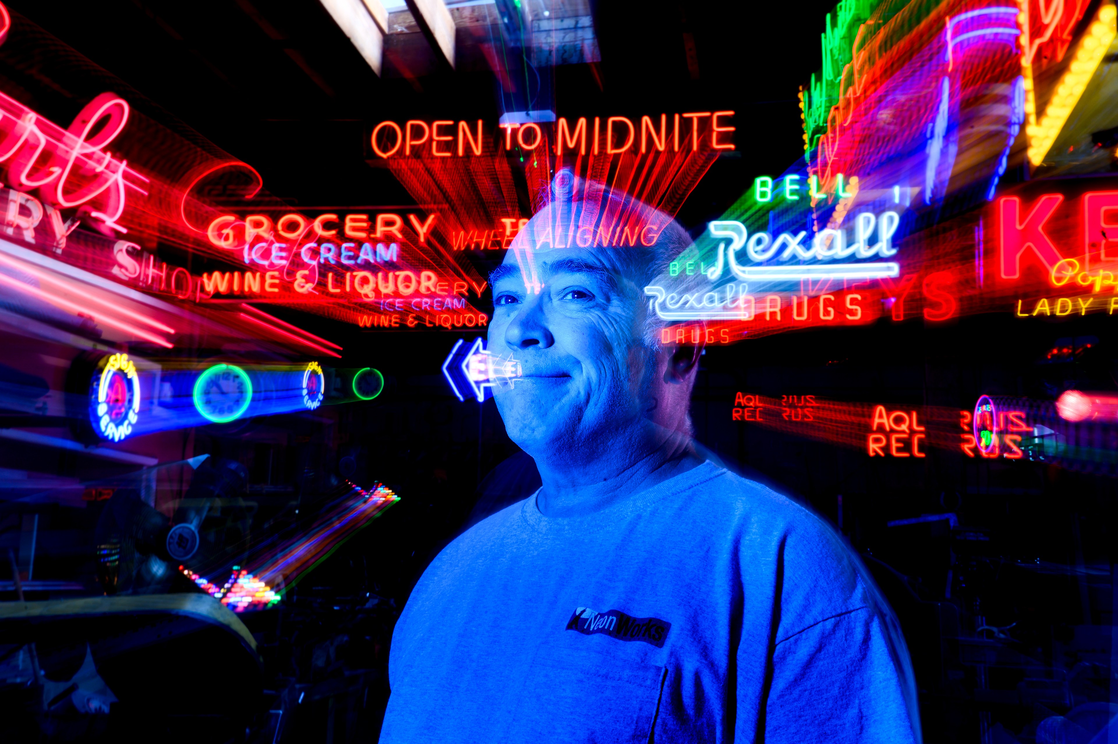 A moody portrait of a man with blue light reflected on him with a variety of fast moving neon signs in the background.