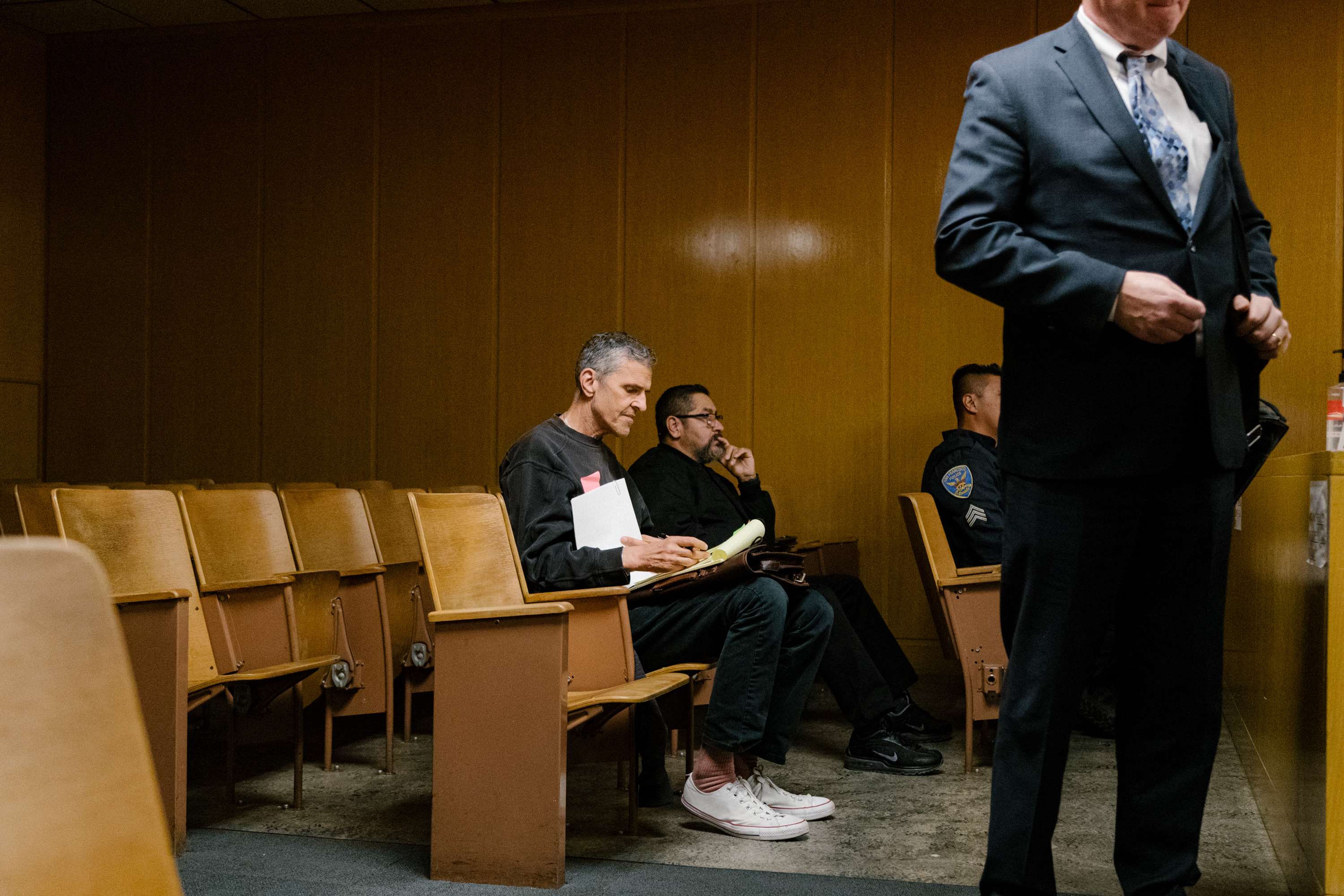 A man sits down in wooden seat in a courtroom setting looking at paperwork.