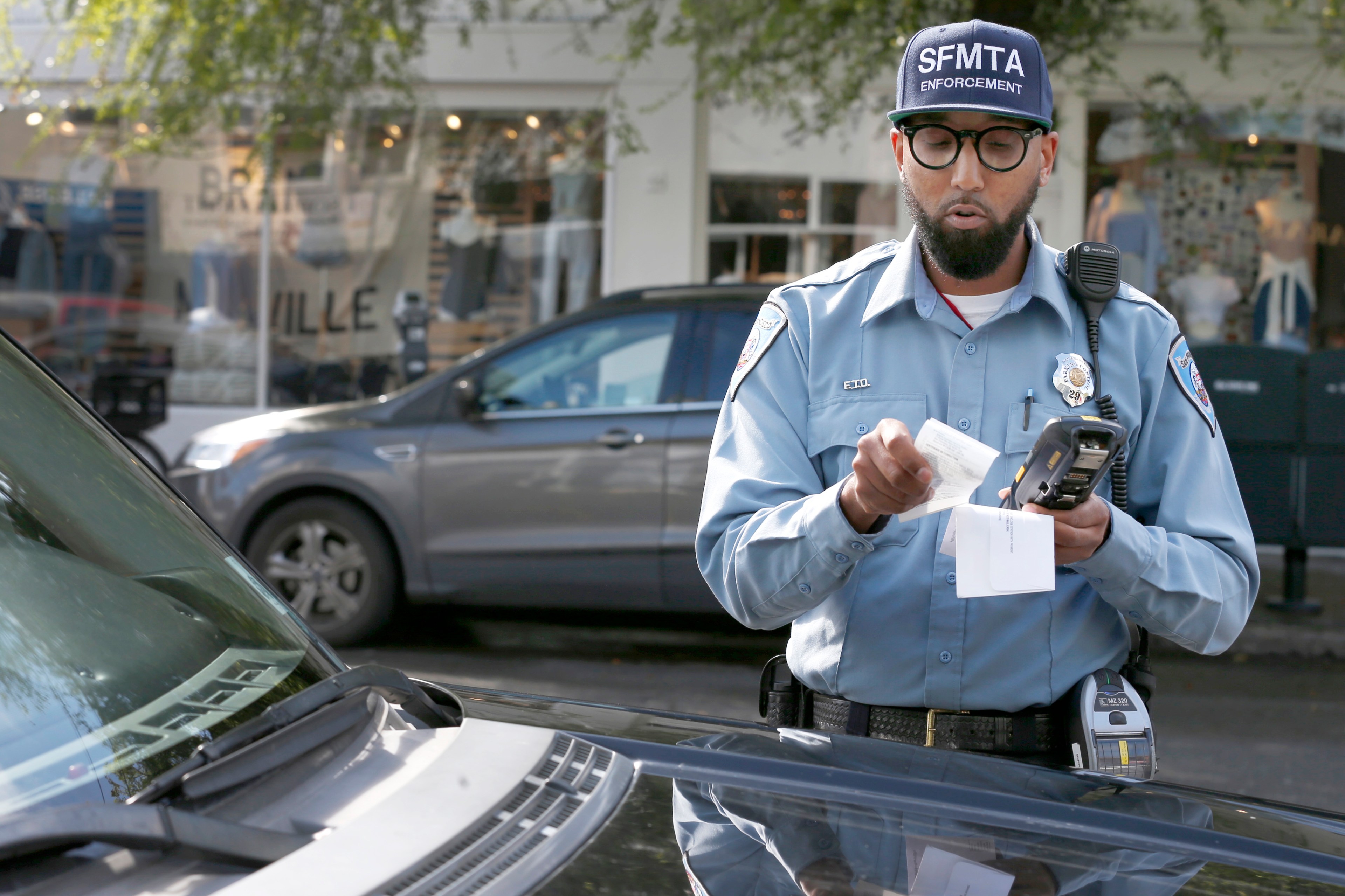 A parking control officer wearing a blue hat issues a parking ticket.