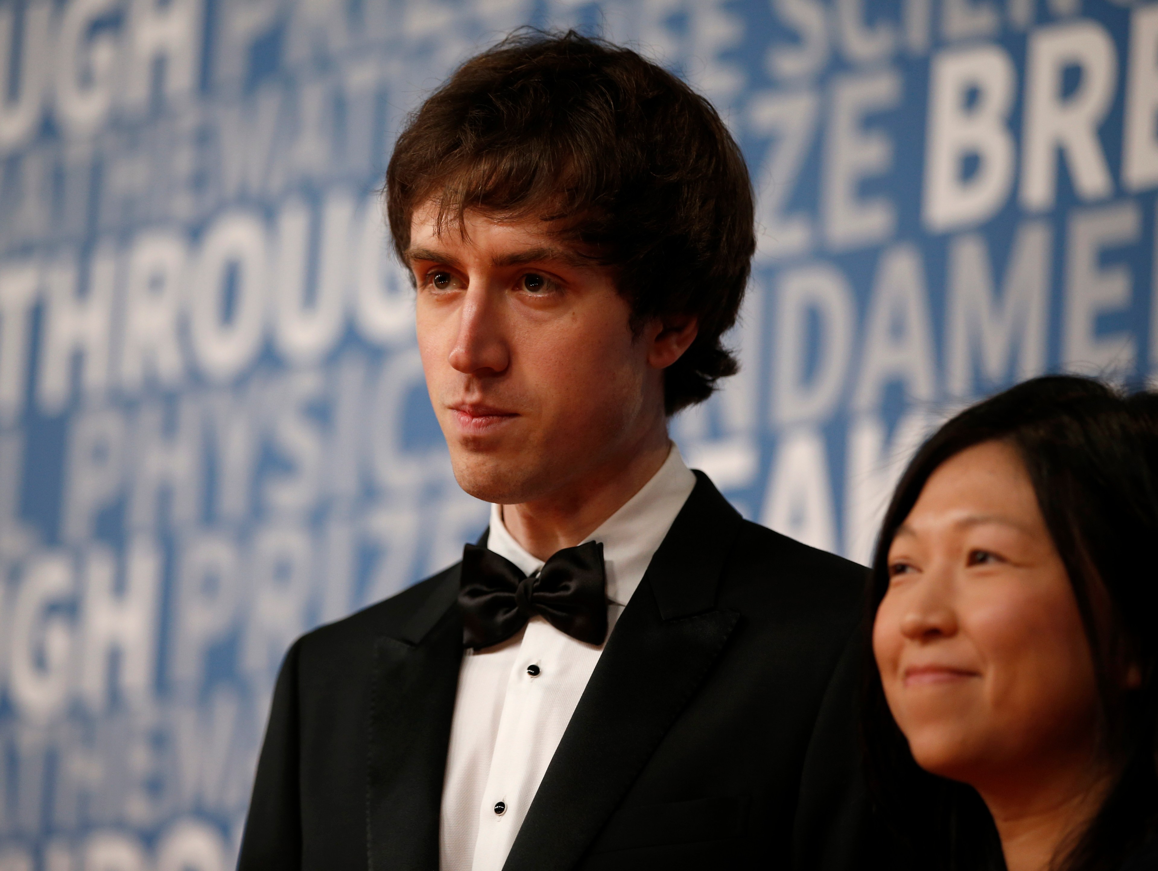 Quora CEO Adam D'Angelo can be seen wearing a black tuxedo, white shirt and a black bowtie. A woman is standing to his left smiling.