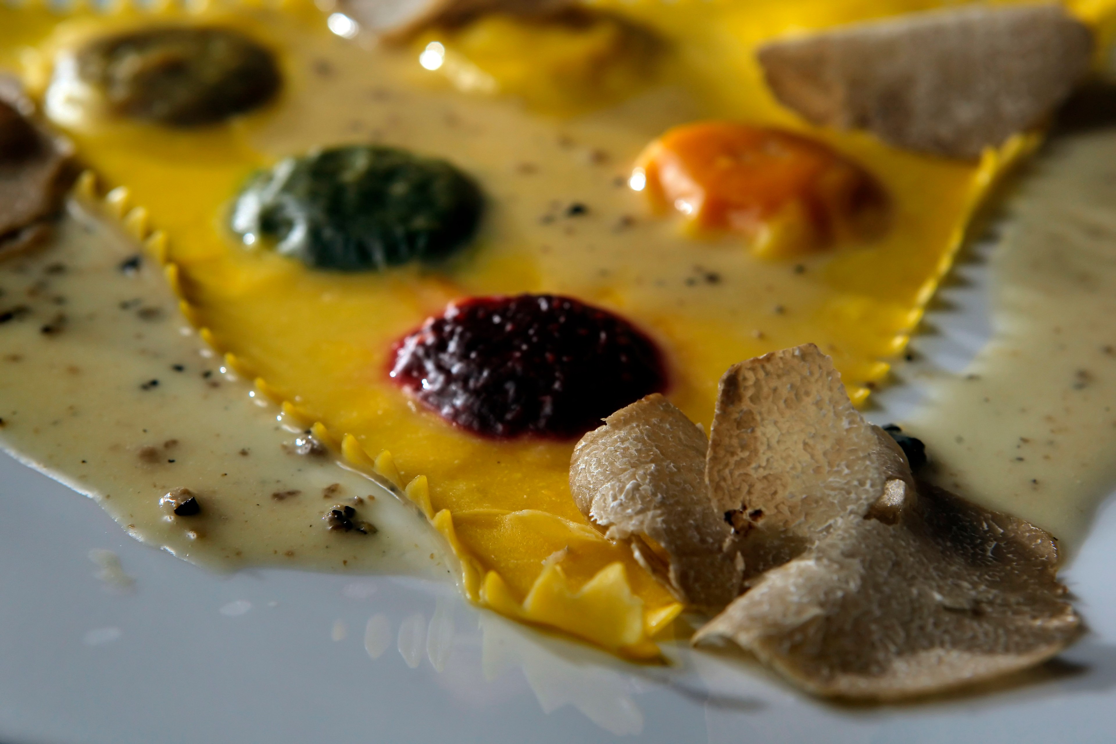 A close-up of ravioli is shown with various sauces and black truffles.