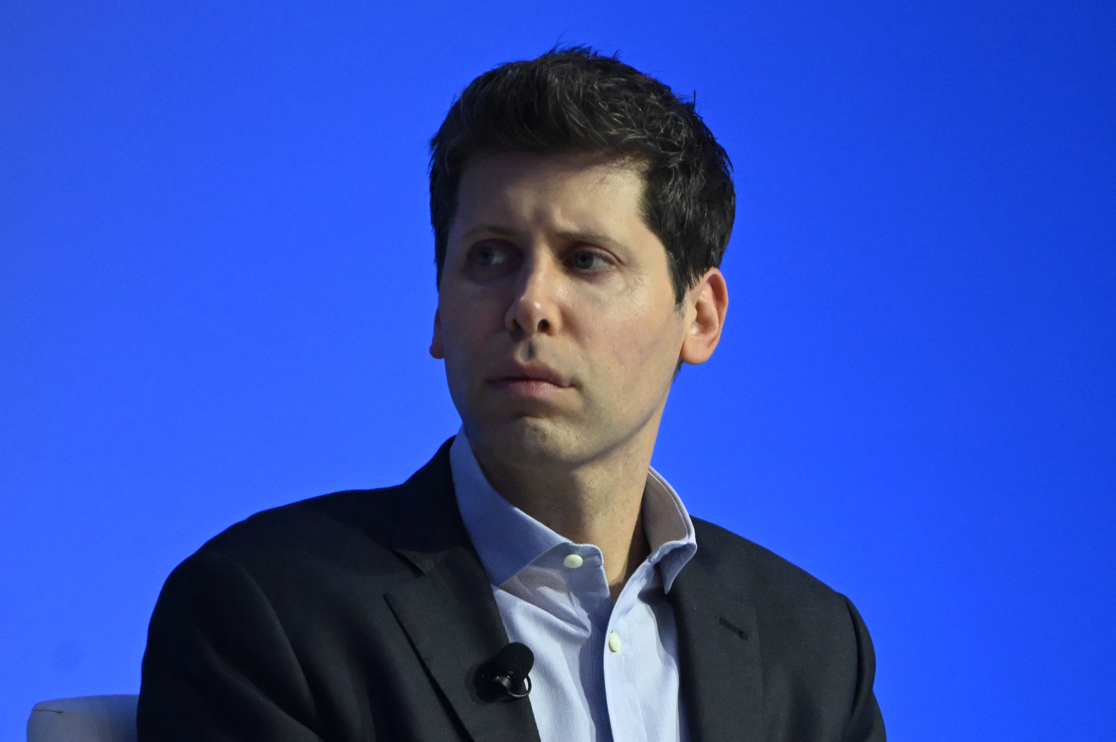 Sam Altman, CEO of OpenAI looks offscreen with a blue background.